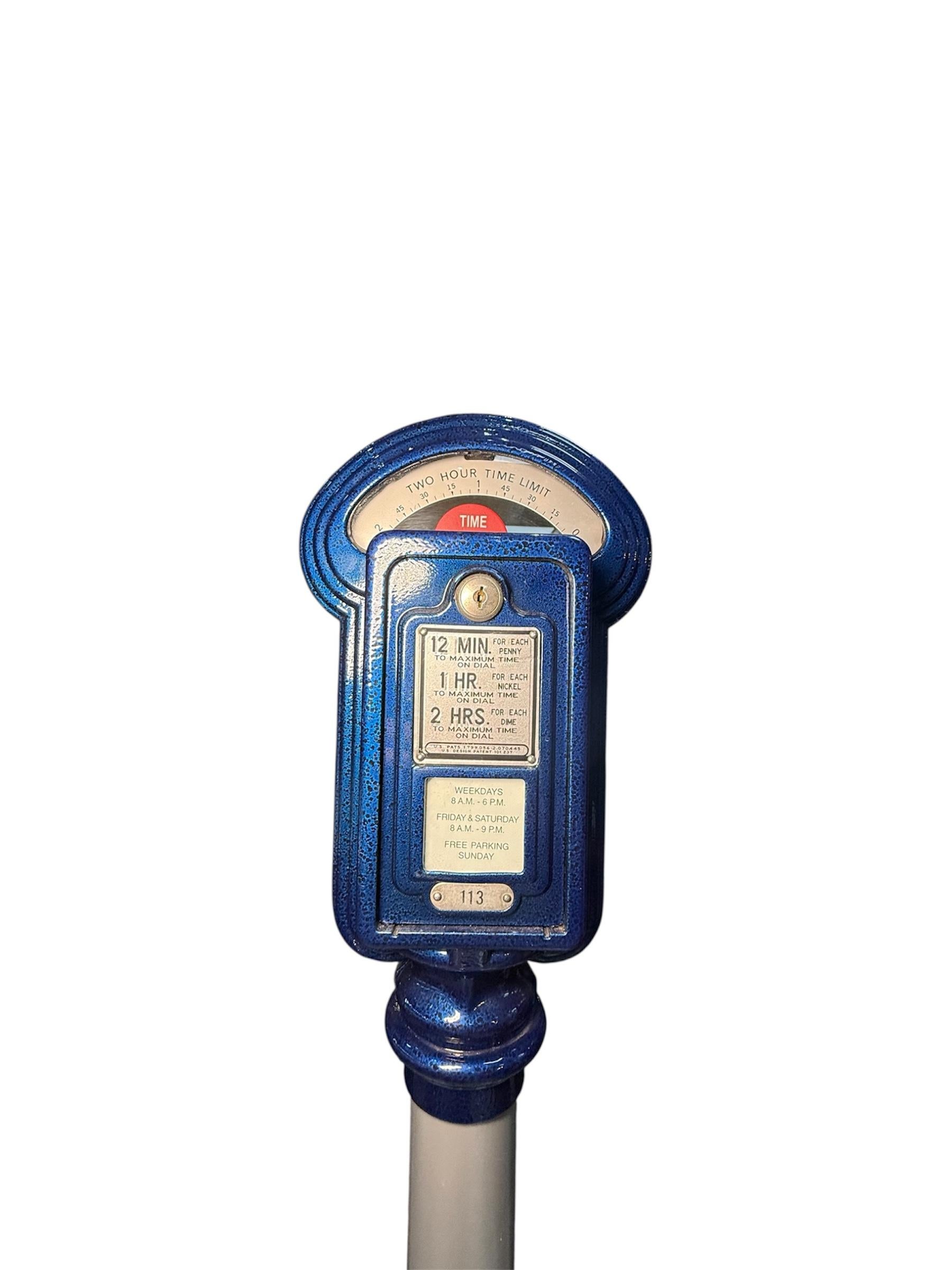 Il s'agit d'un parcmètre Duncan du milieu du 20e siècle. Il s'agit d'un compteur rectangulaire en métal lourd et en verre, peint à la main en bleu royal, dont le sommet arqué est soutenu par une colonne en métal de couleur argentée et par une base