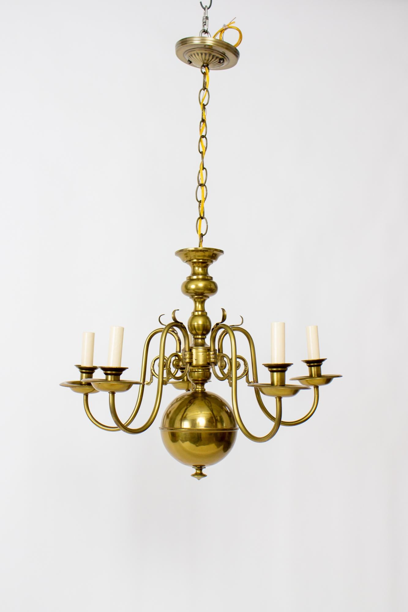 Mid-20th Century dutch colonial style chandelier. All brass with Five arms. Large brass ball at the bottom, with five delicate upsweeping arms. A leafy tuft adorns the uppermost curve of each arm. Center stem is made of brass elements. Includes