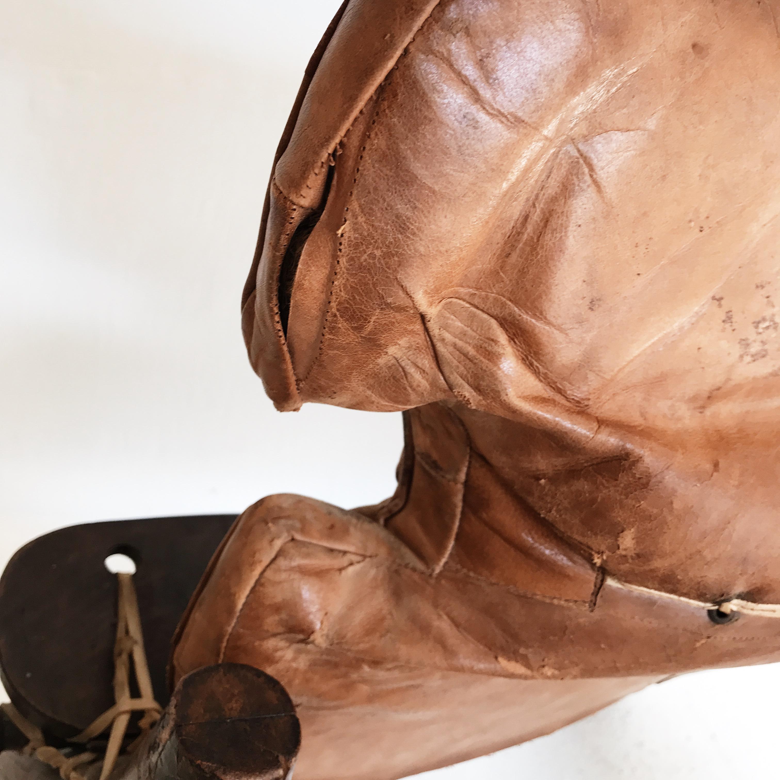 A vintage Egyptian camel saddle footstool. The wooden frame has brass embellishments, including small camel designs on the legs, and the original independent brown leather cushion rested on top.