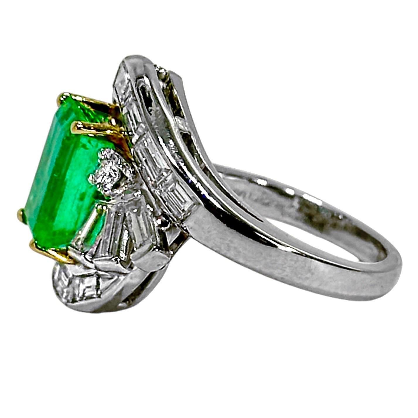 In this classically beautiful Mid-20th Century platinum cocktail ring, artisans have set one emerald cut, natural Colombian emerald surrounded by sixteen straight baguette diamonds, accented with two round brilliant cut diamonds. The center emerald
