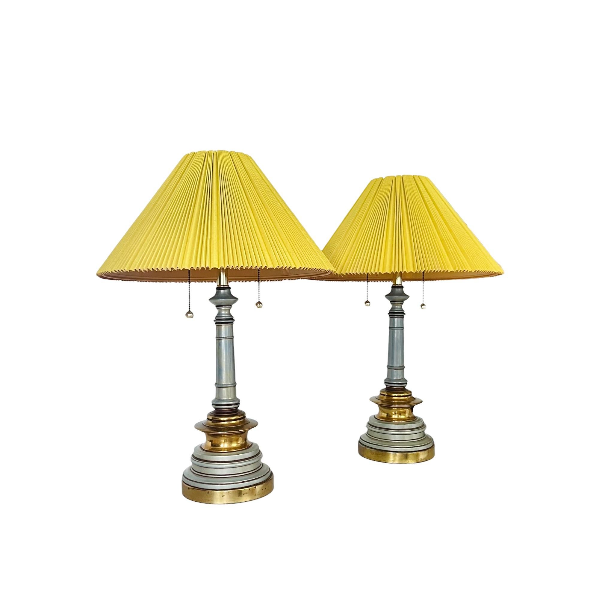 An eclectic mid 20th century pair of Hollywood Regency style enamelwork table lamps with brightly painted shades. Pearlescent blue green enameled body with polished brass details and base. Hardback (plastic under fabric) pleated linen blend lamp