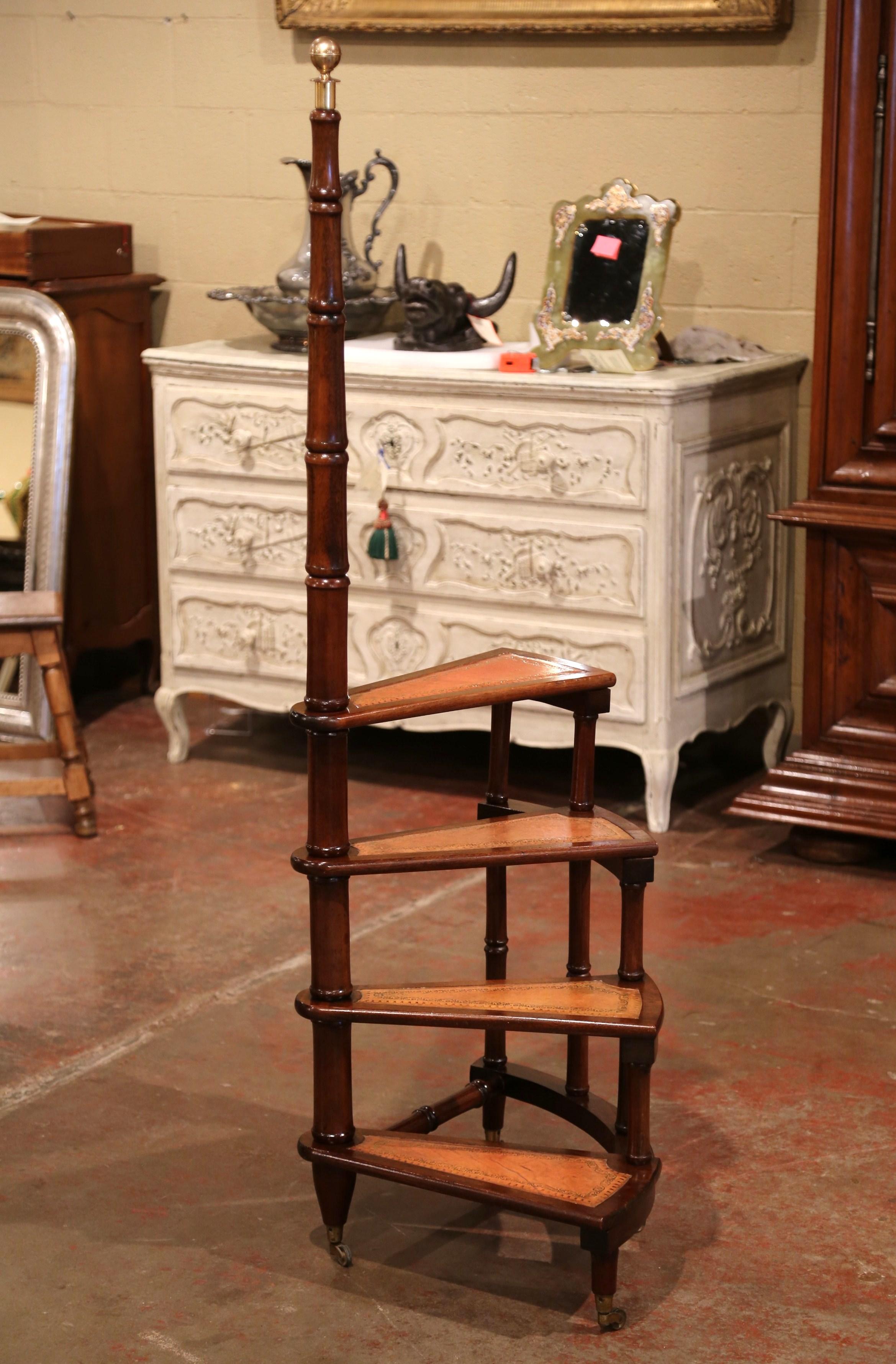 Created in England circa 1960 and standing on four turned legs with bottom wheels, the tall circular step ladder features four stairs rolled around a turned, central post embellished with a decorative brass finial at the pediment. Each step is