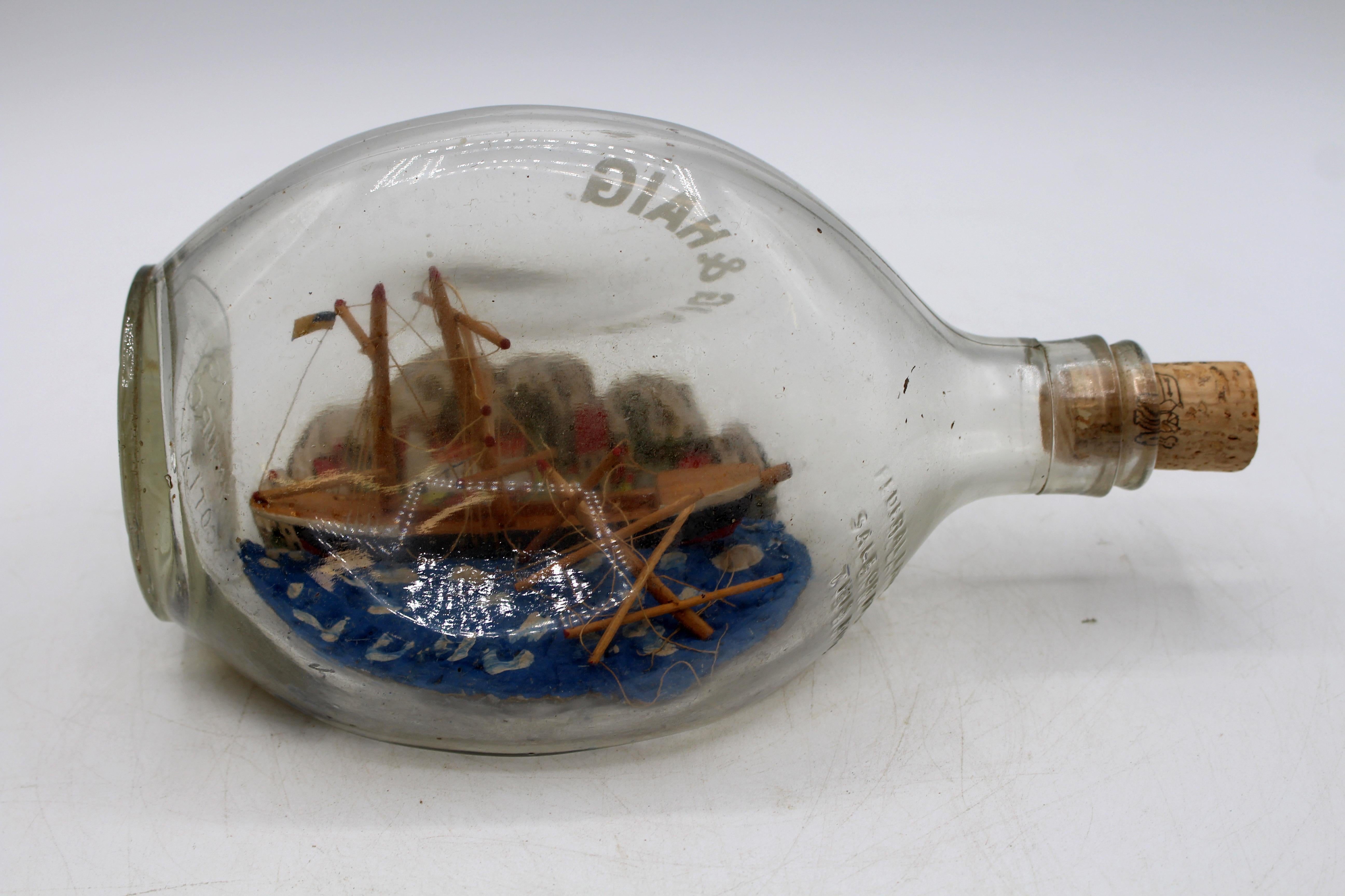 Mid-20th century model of a ship wreck in a bottle, English. Haig & Haig printed & in the glass. Greyish glass. An American ship dashed against a French Village on a rocky coast. Very unusual.
8 3/8