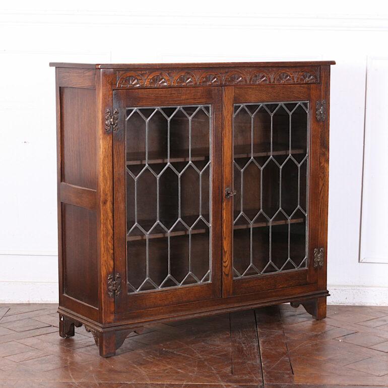 English oak bookcase with a pair of leaded glass doors and with carved details to the top. 


    