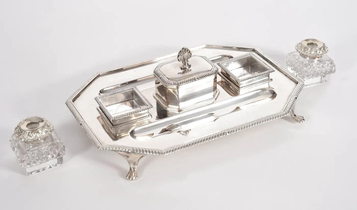 Un'elegante base da scrittura inglese della metà del XX secolo, placcata in argento e completa di due calamai in vetro tagliato. Progettato nel raffinato stile di George III, il pezzo presenta dettagli decorativi finemente incisi e poggia
