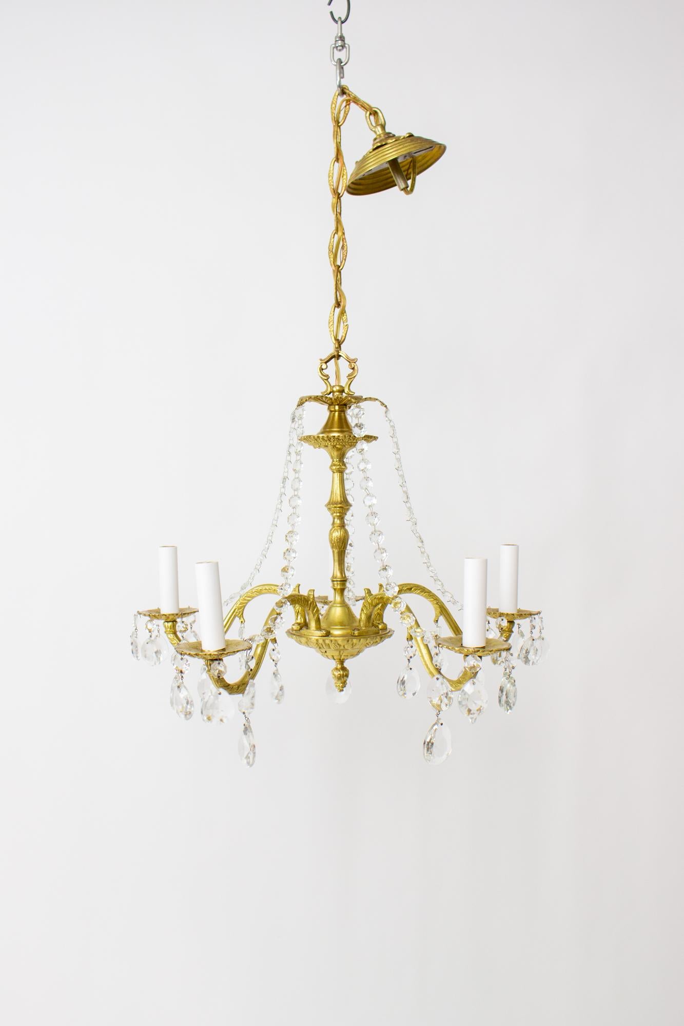 Cast brass and crystal chandelier. Nicely cast brass arms, stem and body. Five arms, with crystals hanging below each light around the cast brass bobeche. Strands of crystals drape from the crown down towards the arms. Brass has been cleaned,