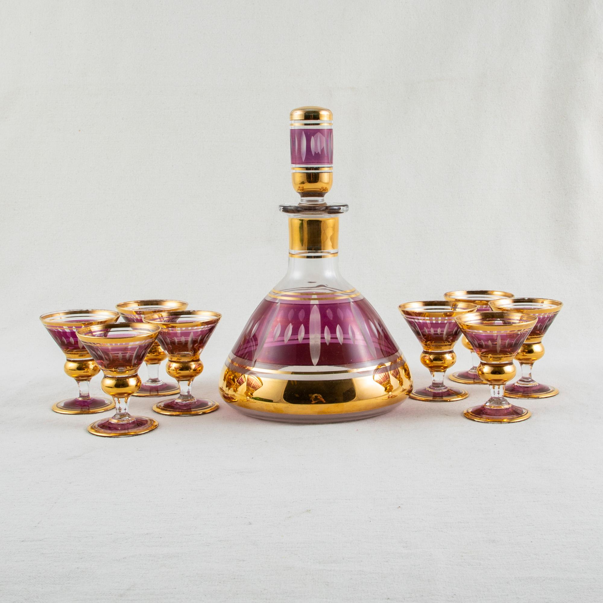 This mid-twentieth century French Art Deco period crystal liqueur service includes eight glasses and one carafe with stopper. The glasses and carafe are tinted with a band of purple and are detailed with bands of gold. Each glass measures 2.5 inches