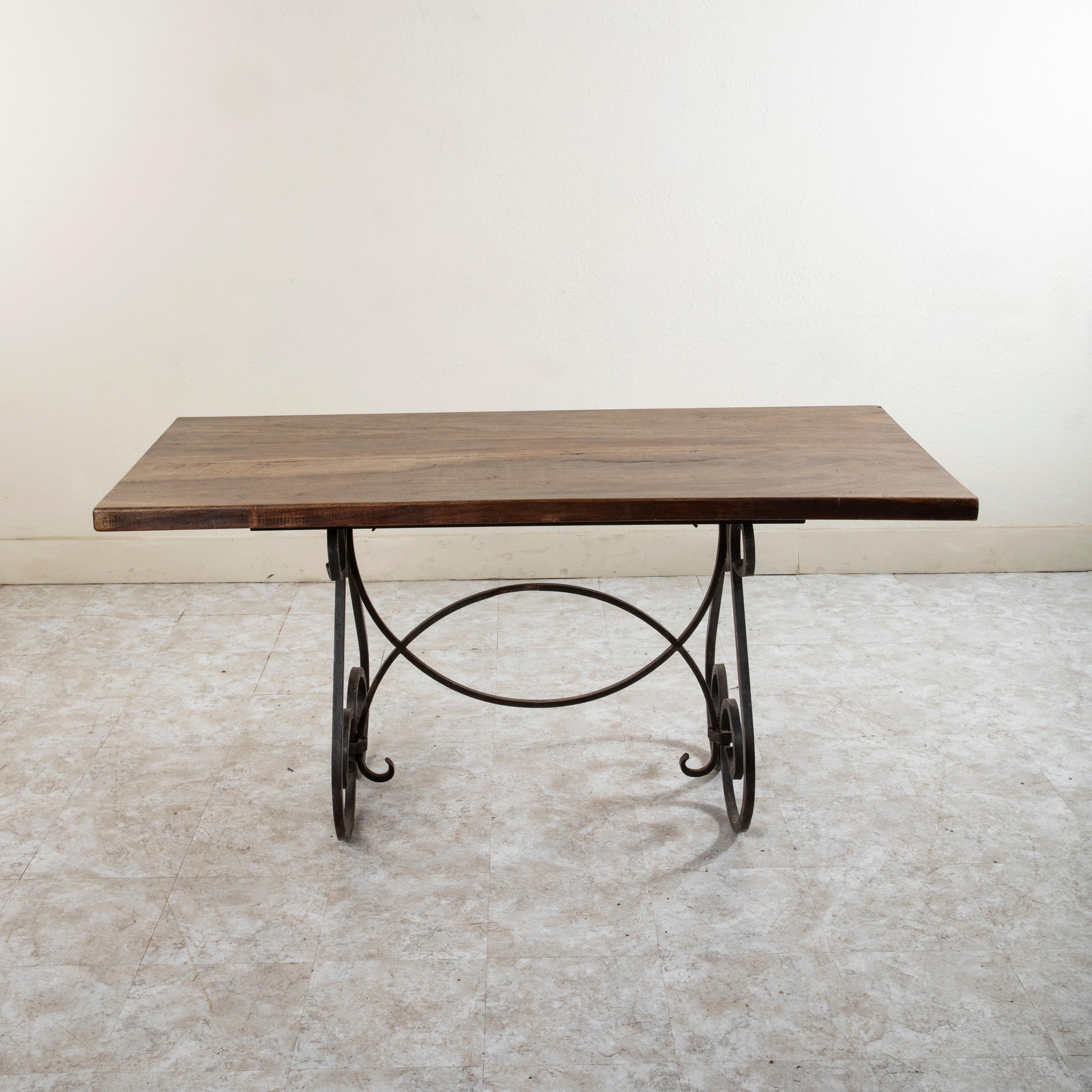 This mid twentieth century French artisan made table features a solid 1.75 inch thick walnut top made from two planks of wood. The table top rests on an iron base with scrolled legs at each end joined by a stretcher formed by two overlapping half