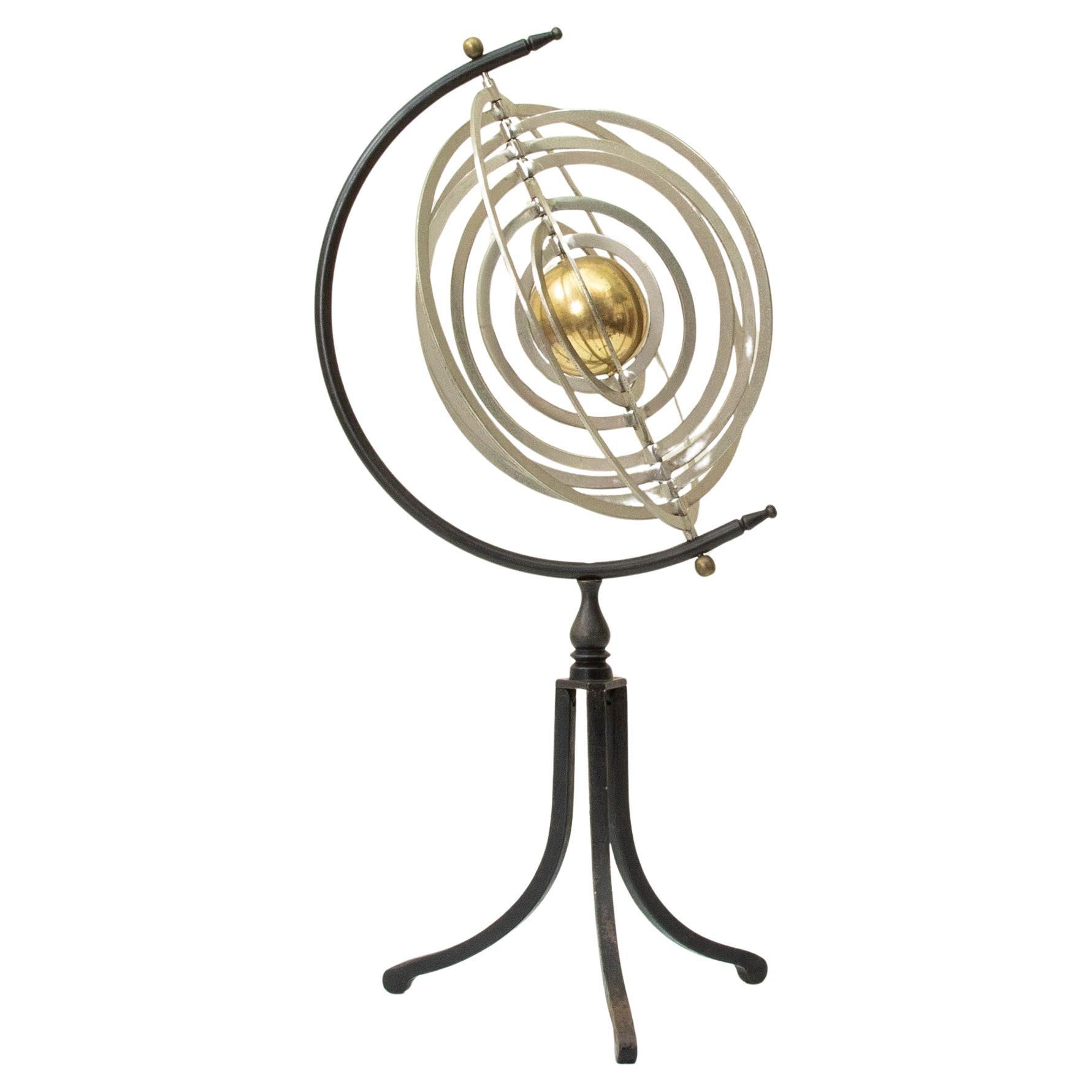 This mid twentieth century French armillary sphere features a central brass globe surrounded by nine concentric steel rings. The rings swivel on a central axis finished with a brass final at each end. The piece rests on a simple iron tripod base. A