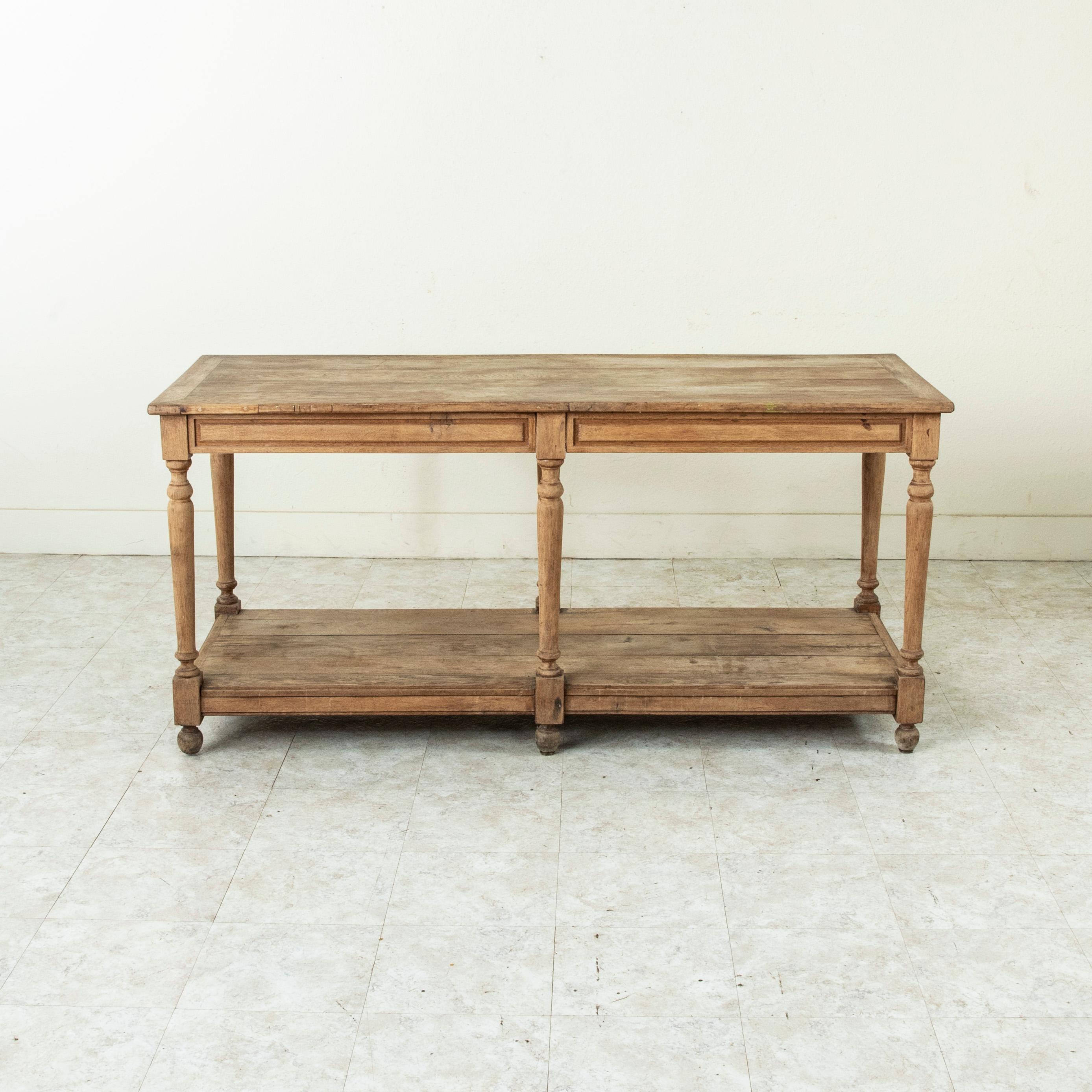Originally used in a French fabric store to lay out and cut fabric, this mid-twentieth century bleached oak silk trader's table rests on tapered turned legs which support its lower shelf. This draper's table, with its lower shelf for storage or