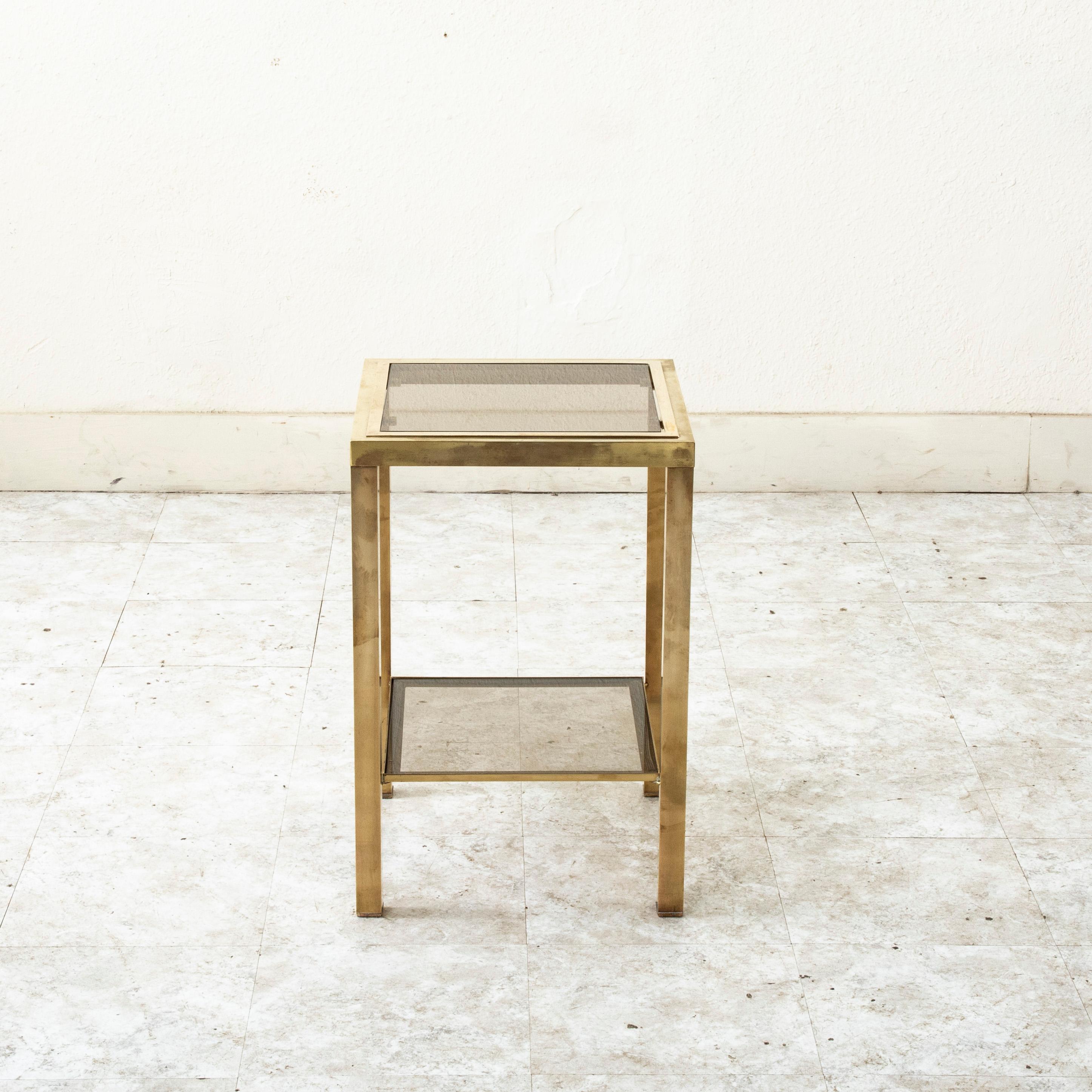 Cette table d'appoint ou d'extrémité carrée en laiton de style français du milieu du siècle comporte deux niveaux dotés de verre fumé qui créent un espace d'exposition unique. Table d'appoint idéale à côté d'une chaise avec ses lignes simples et