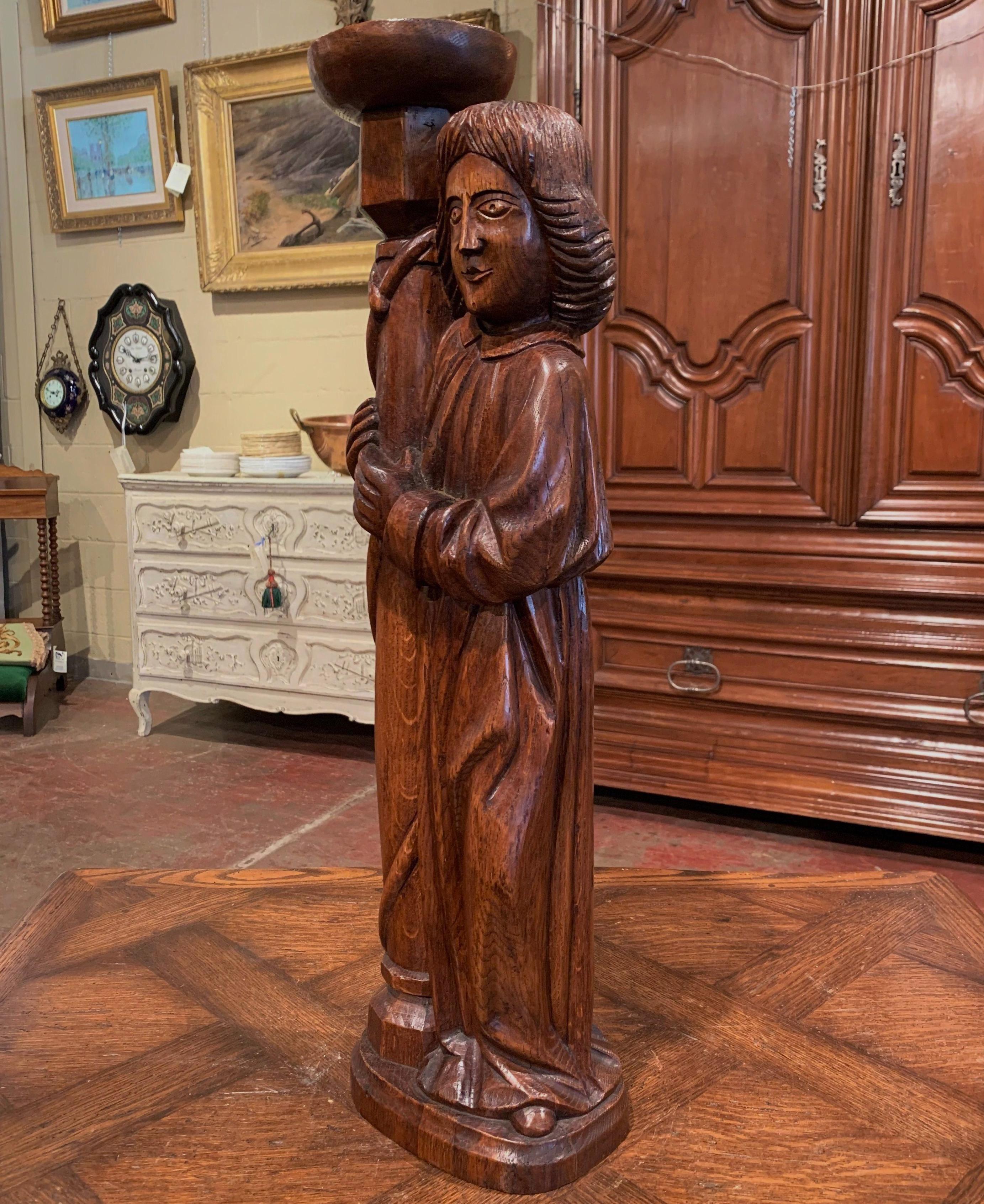 This large antique wood carved sculpture composition was crafted in France circa 1950; made of oakwood, the statue depicts a church page or altar server holding a torch. The top for the candlestick is curved in order to hold a candle. The carved
