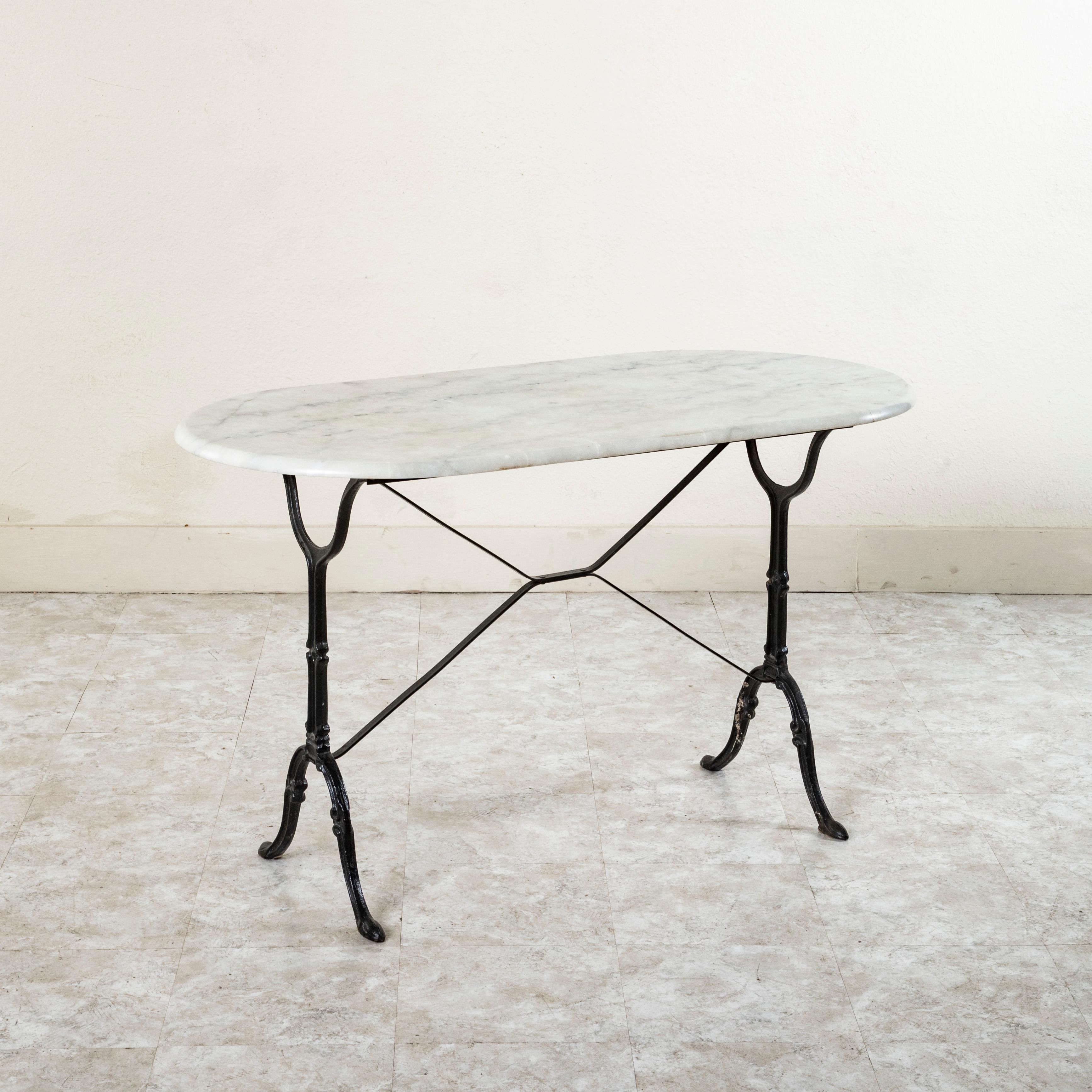 Originally used in a French brasserie in the mid twentieth century, this cast iron bistro table or cafe table features a solid white oval marble top with grey veining. Scrolled iron legs support the top and are joined by an X-stretcher that provides