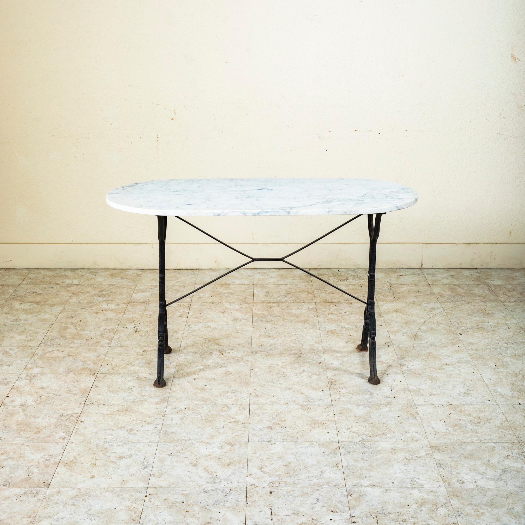 Originally used in a French brasserie in the Mid-20th Century, this cast iron bistro table or cafe table features a solid white marble top. Scrolled iron legs support the top and are joined by an X-stretcher that provides additional stability to the