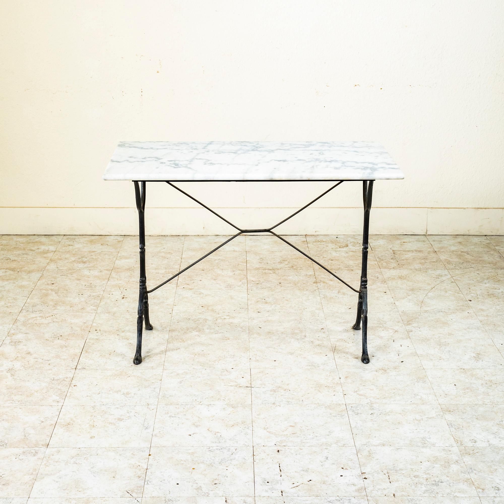 Originally used in a French brasserie during the mid-twentieth century, this cast iron bistro table or cafe table features a solid white marble top with grey veining. Scrolled iron legs support the top and are joined by an X-stretcher that provides