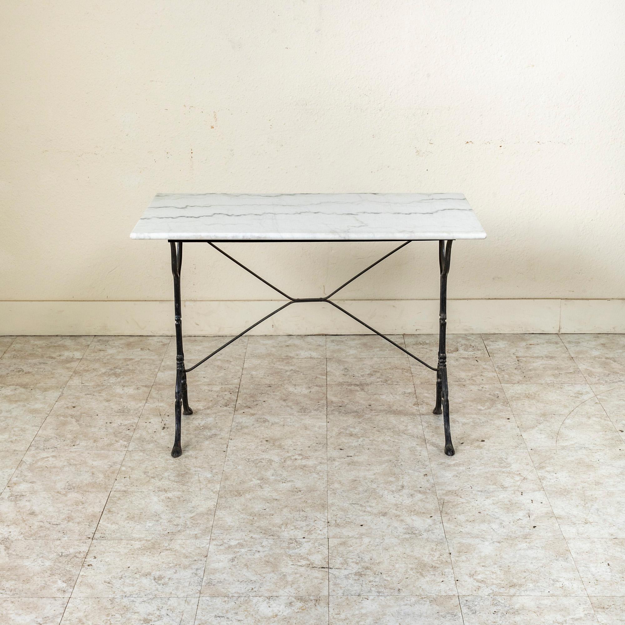 Originally used in a French brasserie during the mid-twentieth century, this cast iron bistro table or cafe table features a solid white marble top with grey veining. Scrolled iron legs support the top and are joined by an X-stretcher that provides