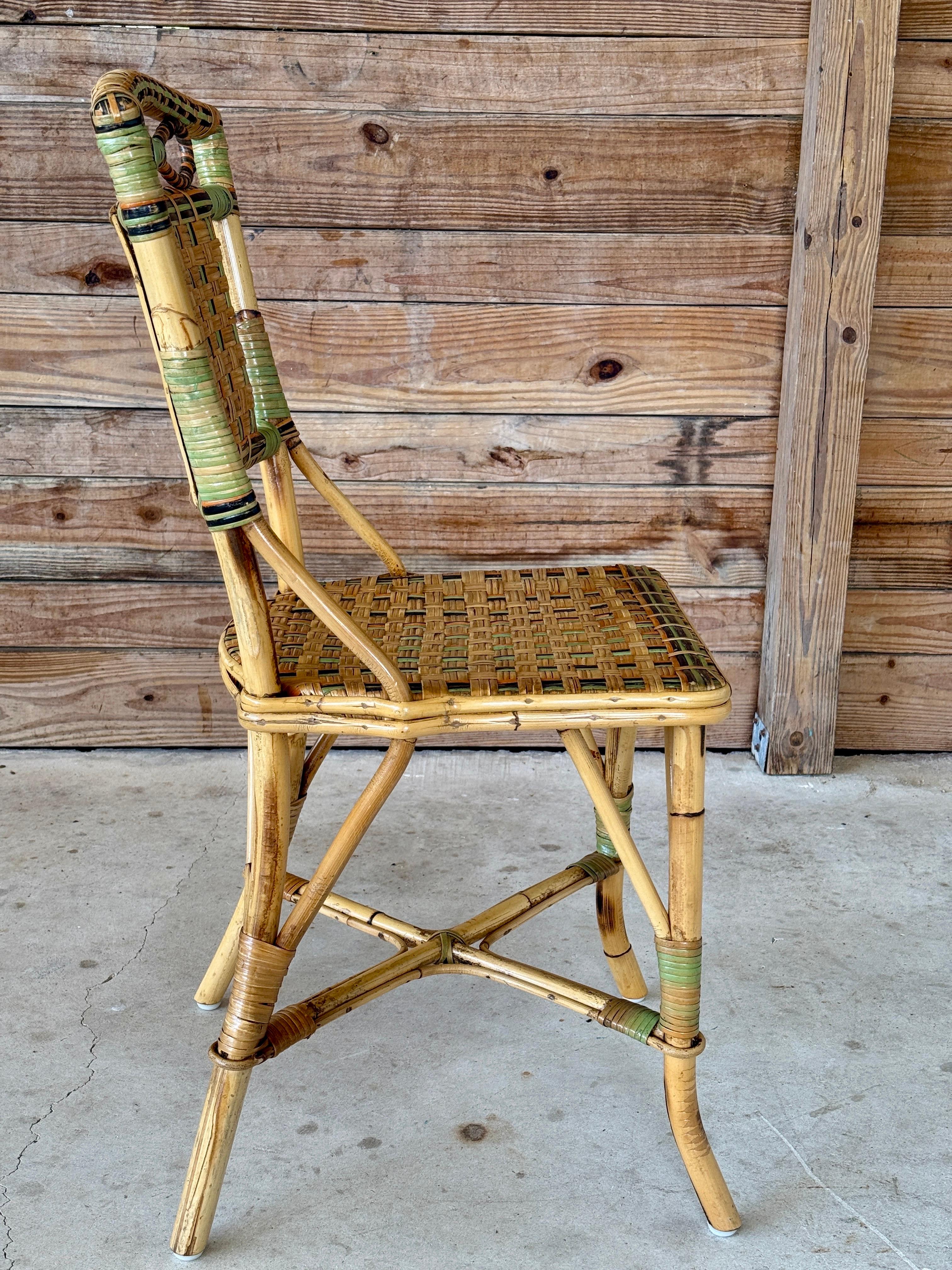 Encantadora silla auxiliar bistro de ratán de mediados del siglo XX, con coloridos detalles tejidos y un escultural lazo en la parte superior. Se ha realizado un ligero repintado para conservar el acabado original y proteger al mismo tiempo su