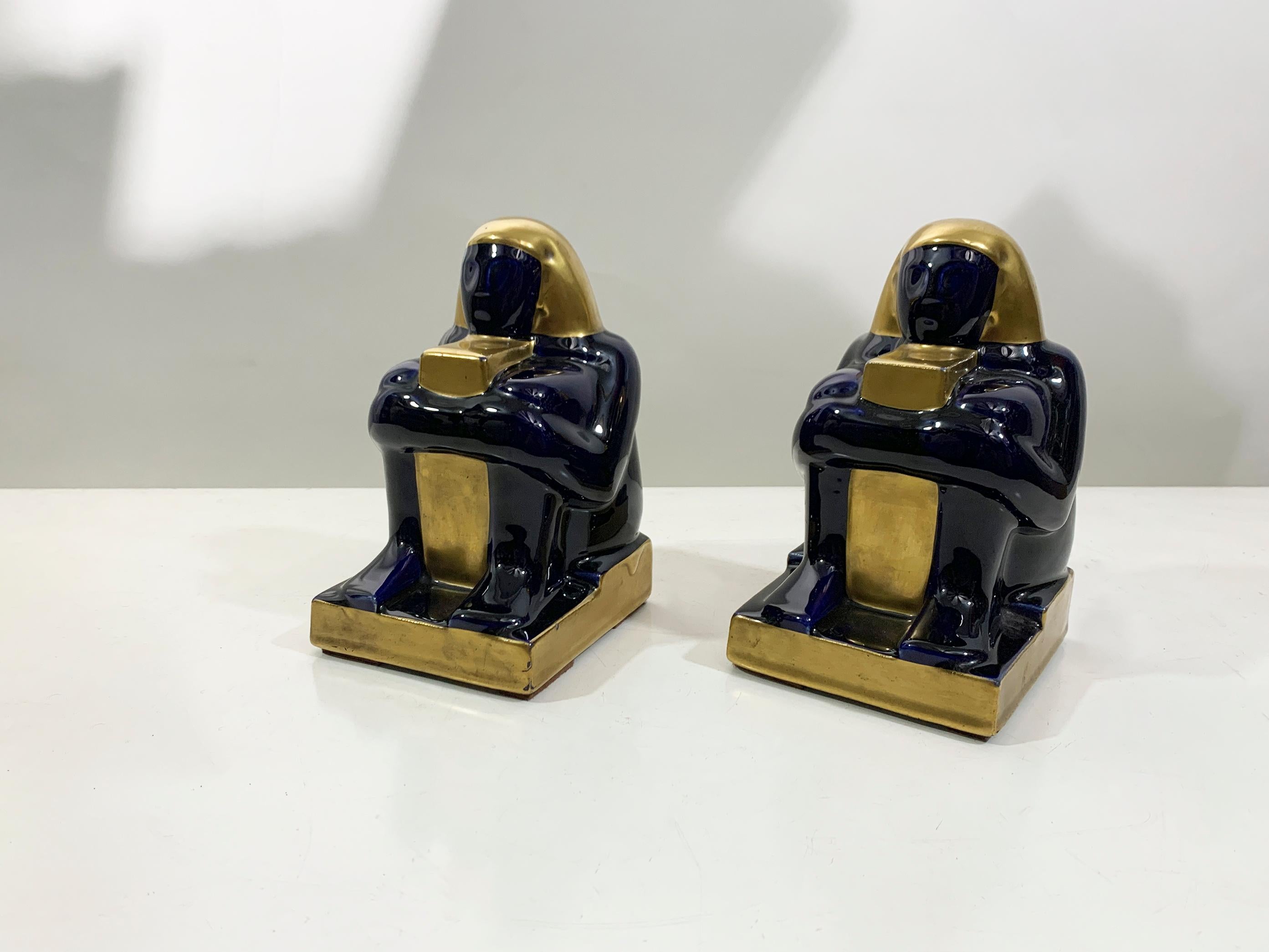 Die auffälligen Buchstützen aus der Mitte des Jahrhunderts im ägyptischen Revival-Stil bestehen aus glasierter Keramik mit einer dramatischen zweifarbigen Palette aus tiefem Marineblau und metallischem Gold. Diese um 1950 in Frankreich hergestellten