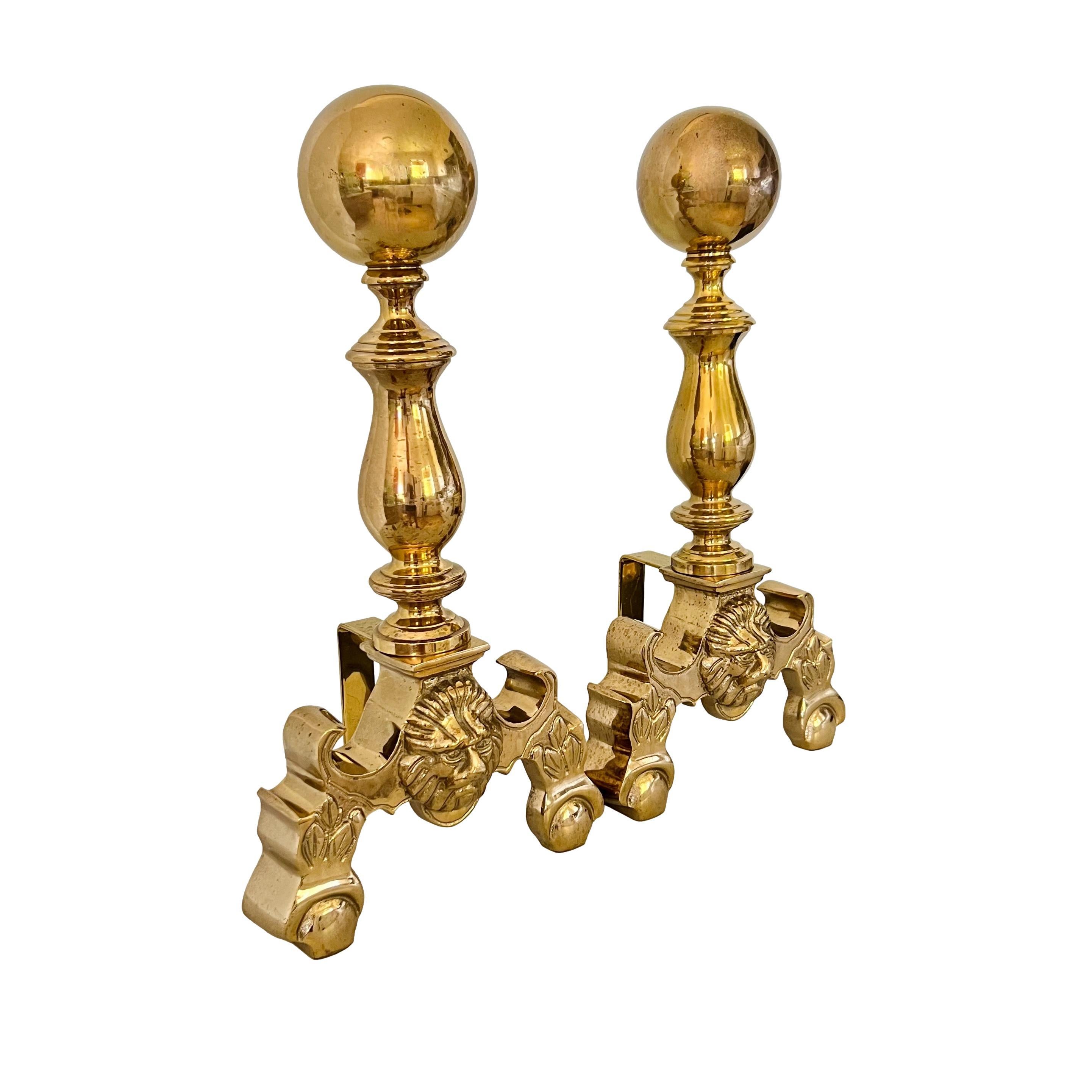 A vintage pair of French Empire style chenets or andirons. Heavy brass featuring neoclassical lion heads and large cannonball toppers. Made by Sunset.

Dimensions: 9