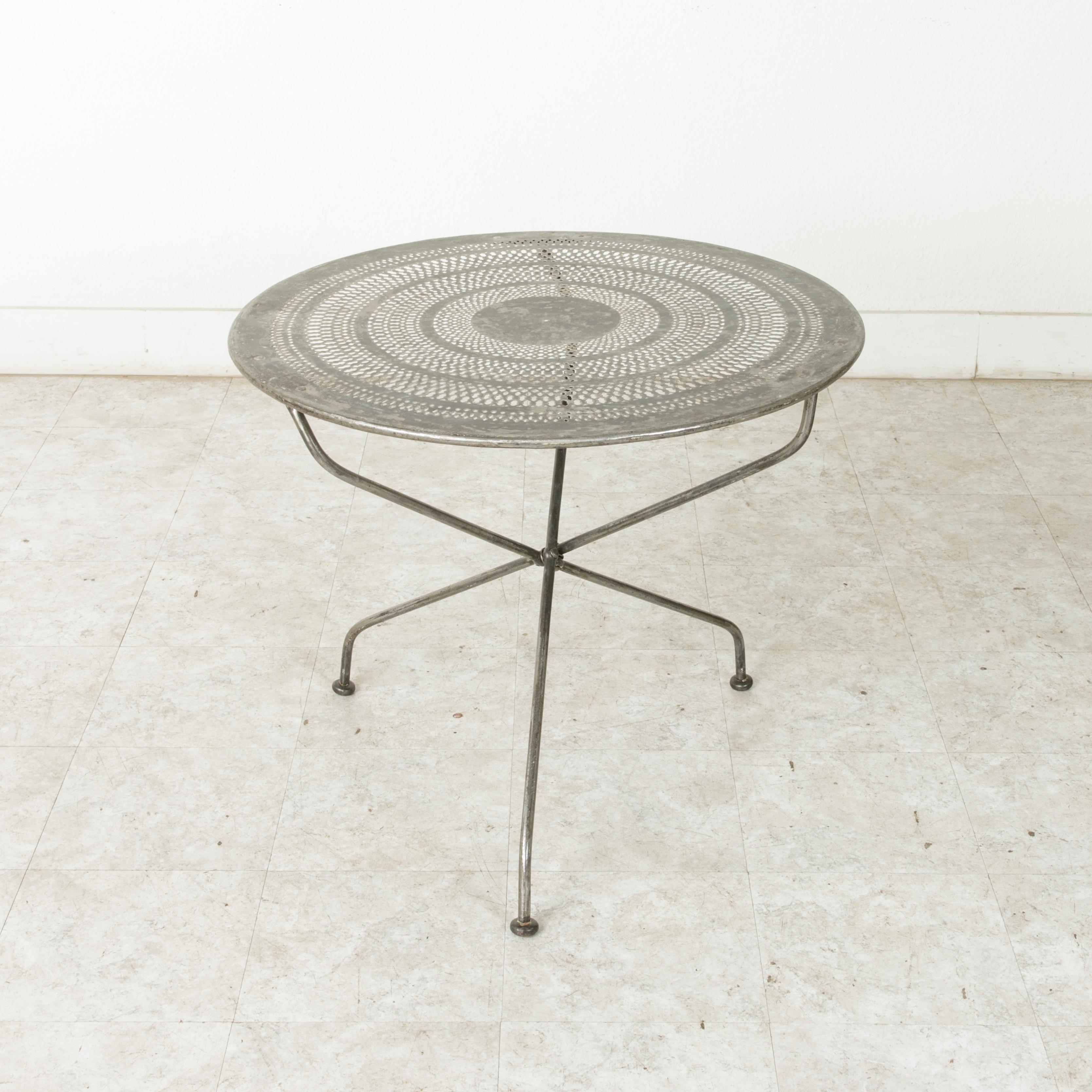 This French round outdoor garden table from the mid-twentieth century features a pierced metal top in a concentric circled pattern. The pierced top allows rainwater to pass through if the table is left outdoors. Resting on three legs that join in