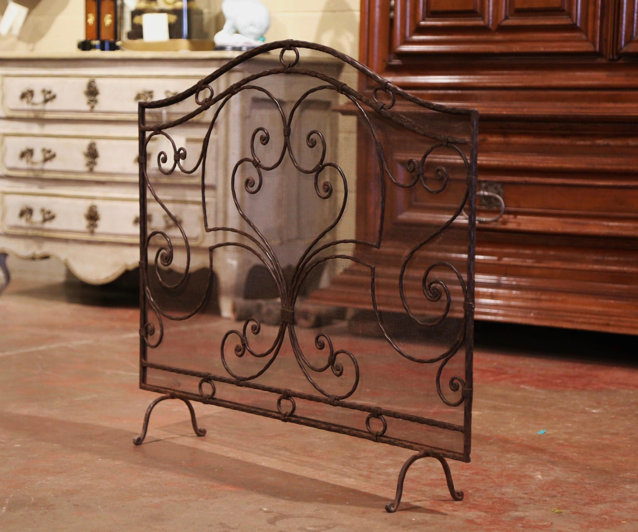 Decorate a fireplace hearth with this elegant iron screen. Created in France circa 1970 and standing on small scrolled feet, the wrought iron piece features an arched top and is decorated with intricate forged scroll motifs. The fireplace essential