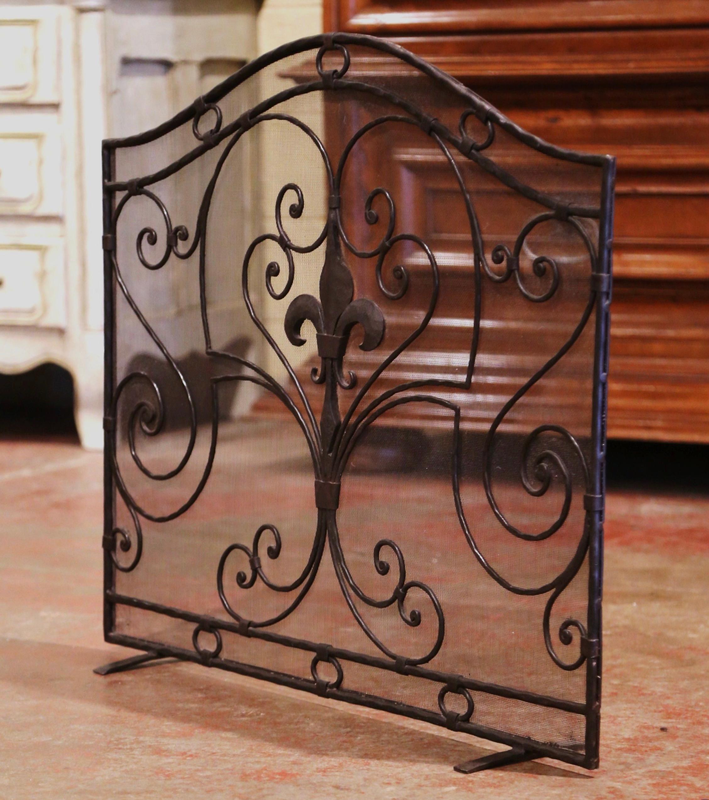 Decorate a fireplace hearth with this elegant iron screen. Created in France circa 1970 and standing on small scrolled feet, the wrought iron piece features an arched top and is decorated with intricate forged scroll motifs, including a large