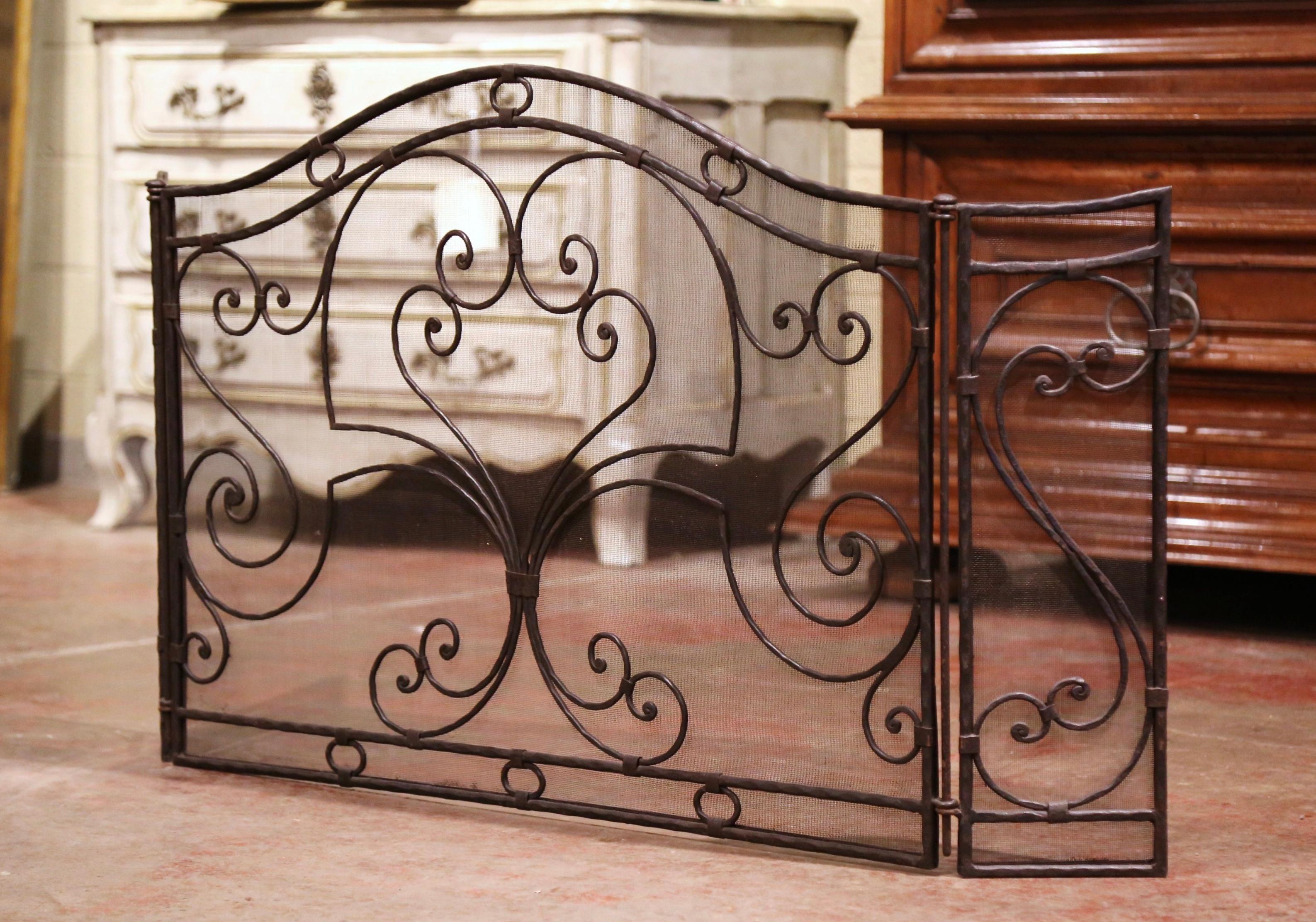 Decorate a fireplace hearth with this elegant arched screen. Forged in France, circa 1970, the freestanding hand forged screen features three panels with heavy scroll work decor; it is further embellished by a protective metal mesh screen on each