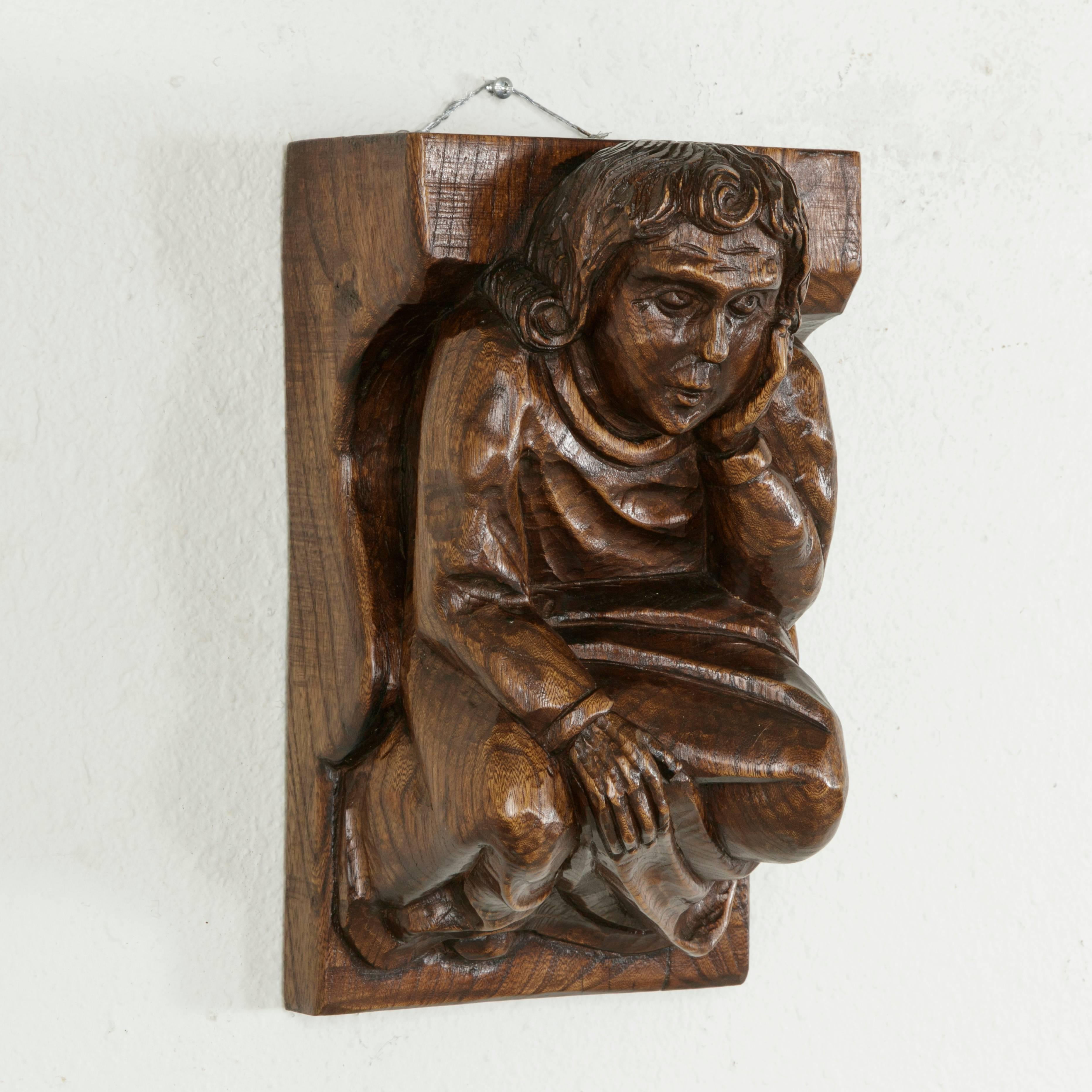 This midcentury French solid elm wall sconce was originally placed under a ceiling beam for support and features a hand carved medieval figure. Dressed in a simple robe, the medieval man rests his head on his left hand in a pensive pose while his