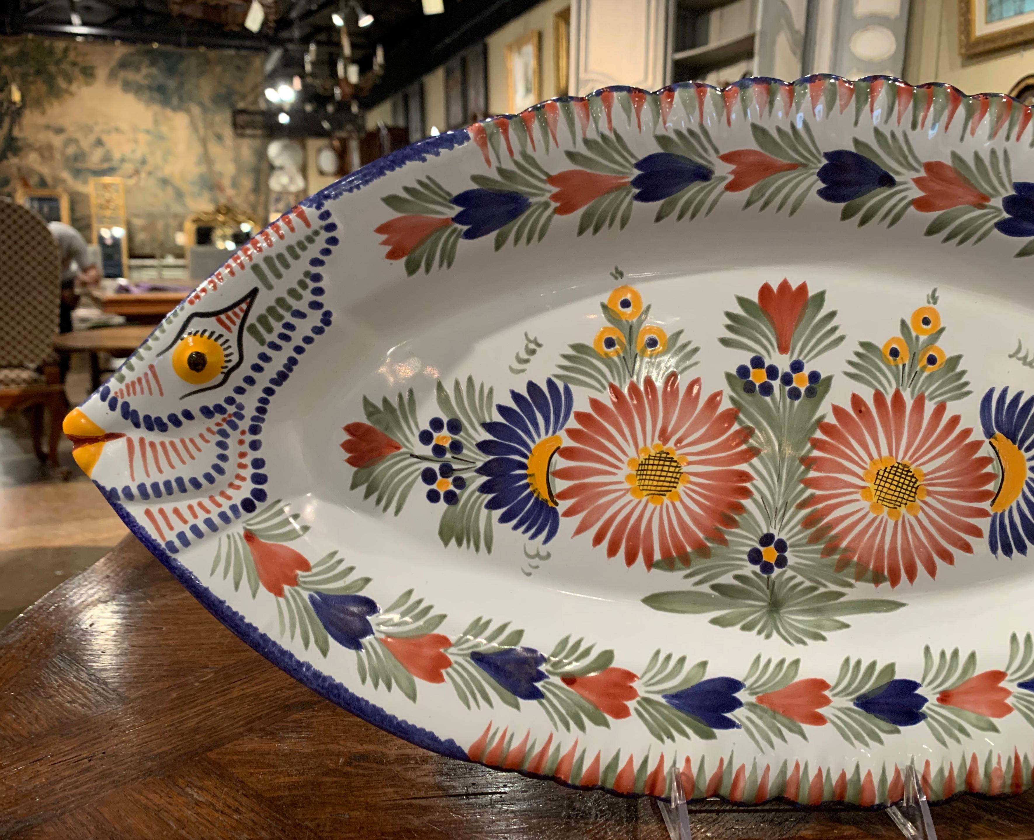 This colorful ceramic platter was created in Brittany, France, circa 1950. Shaped as a fish, the large tray is decorated with hand painted floral motifs in the blue, red and yellow palette over a white background. The serving piece is in excellent