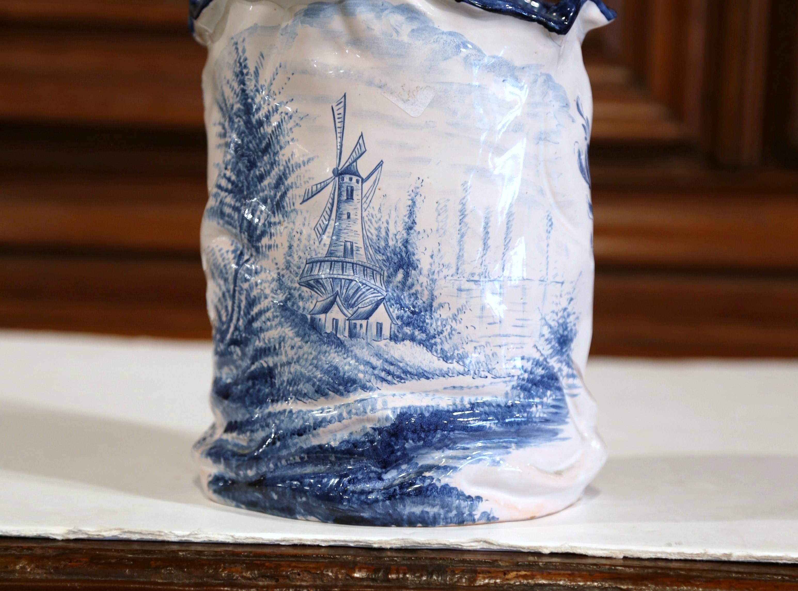 This antique planter was created in France, circa 1950. Hand-painted in a blue and white Delft style, the porcelain cache pot has an oval shape and features the traditional windmill on one side and fisherman in his boat on the other. The classic
