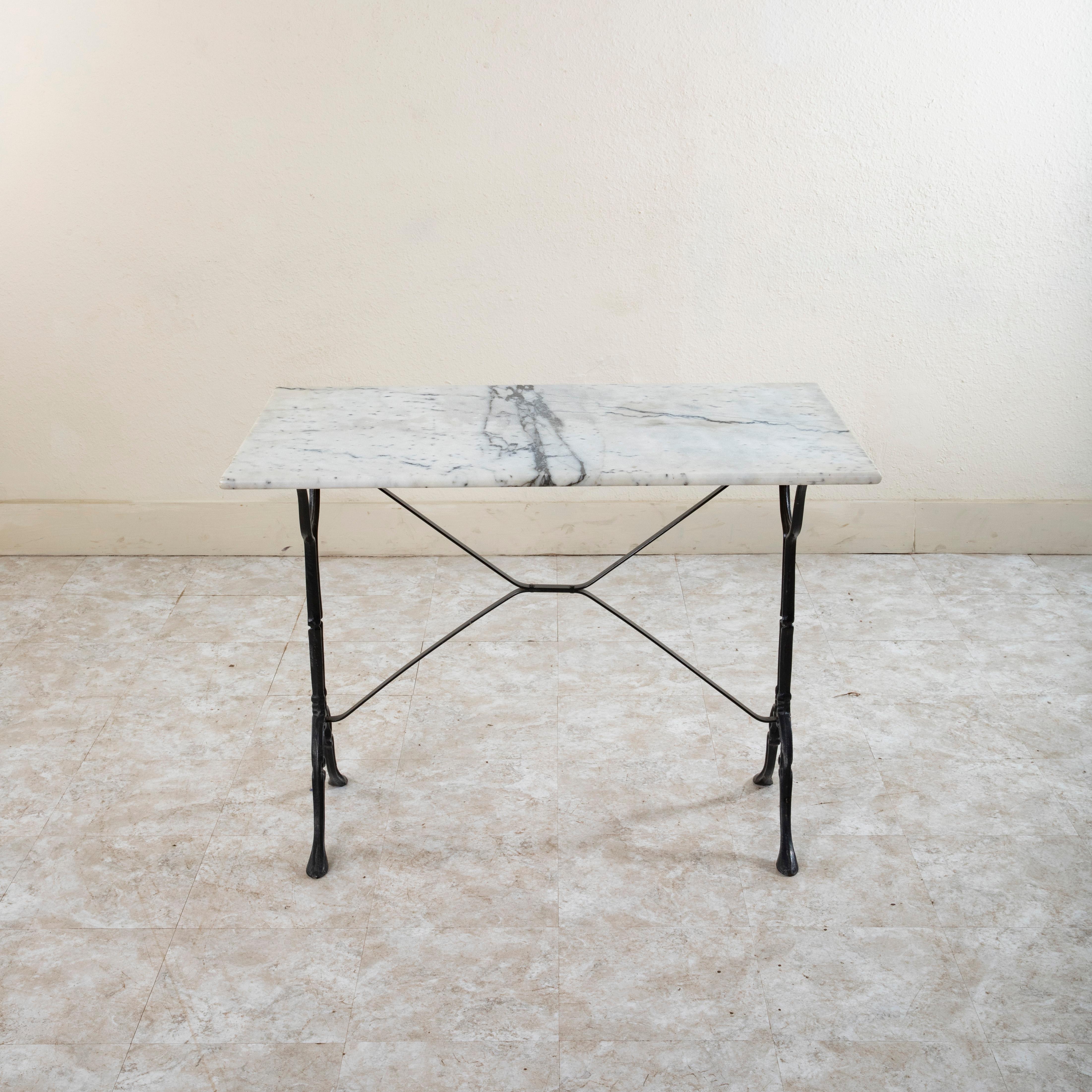 Originally used in a French brasserie during the mid-twentieth century, this cast iron bistro table or cafe table features a solid white marble top with grey veining. Scrolled iron legs support the top and are joined by an X-stretcher that provides