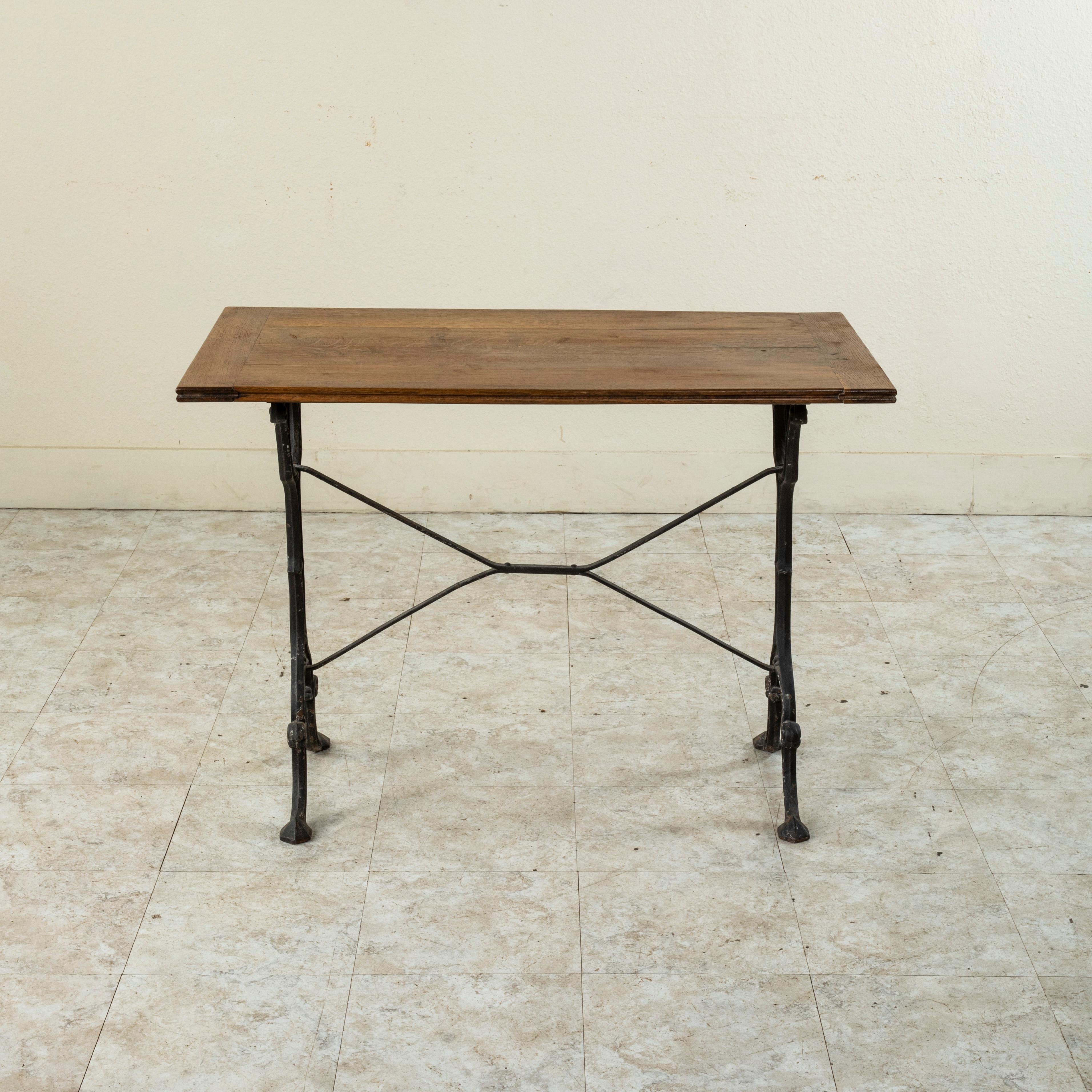 Originally used in a French brasserie during the Mid-20th Century, this cast iron bistro table or cafe table features a beveled oak top. Scrolled iron legs support the top and are joined by an X-stretcher that provides additional stability to the