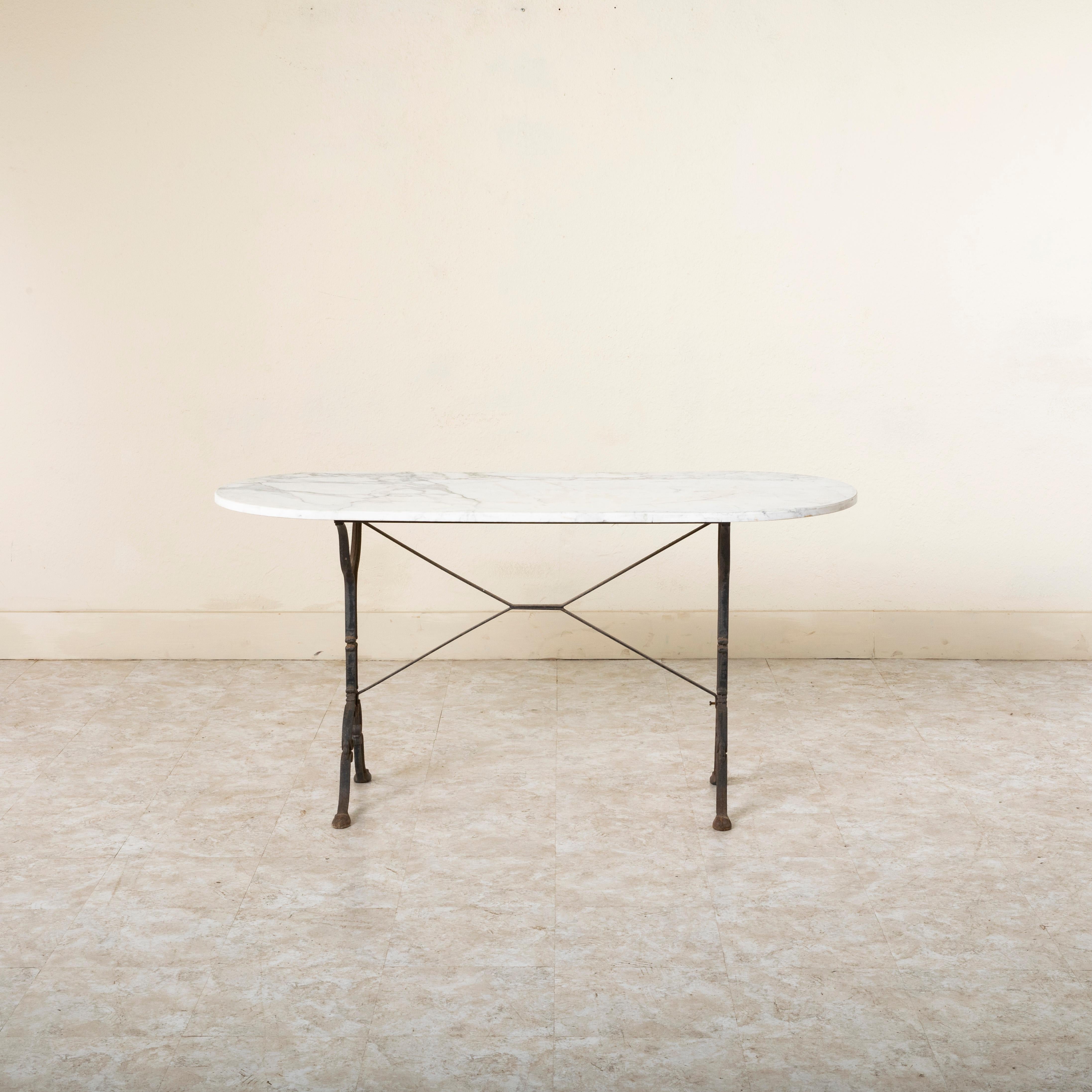 Originally used in a French brasserie in the mid twentieth century, this cast iron bistro table or cafe table features a solid white oval marble top with grey veining. Scrolled iron legs support the top and are joined by an X-stretcher that provides