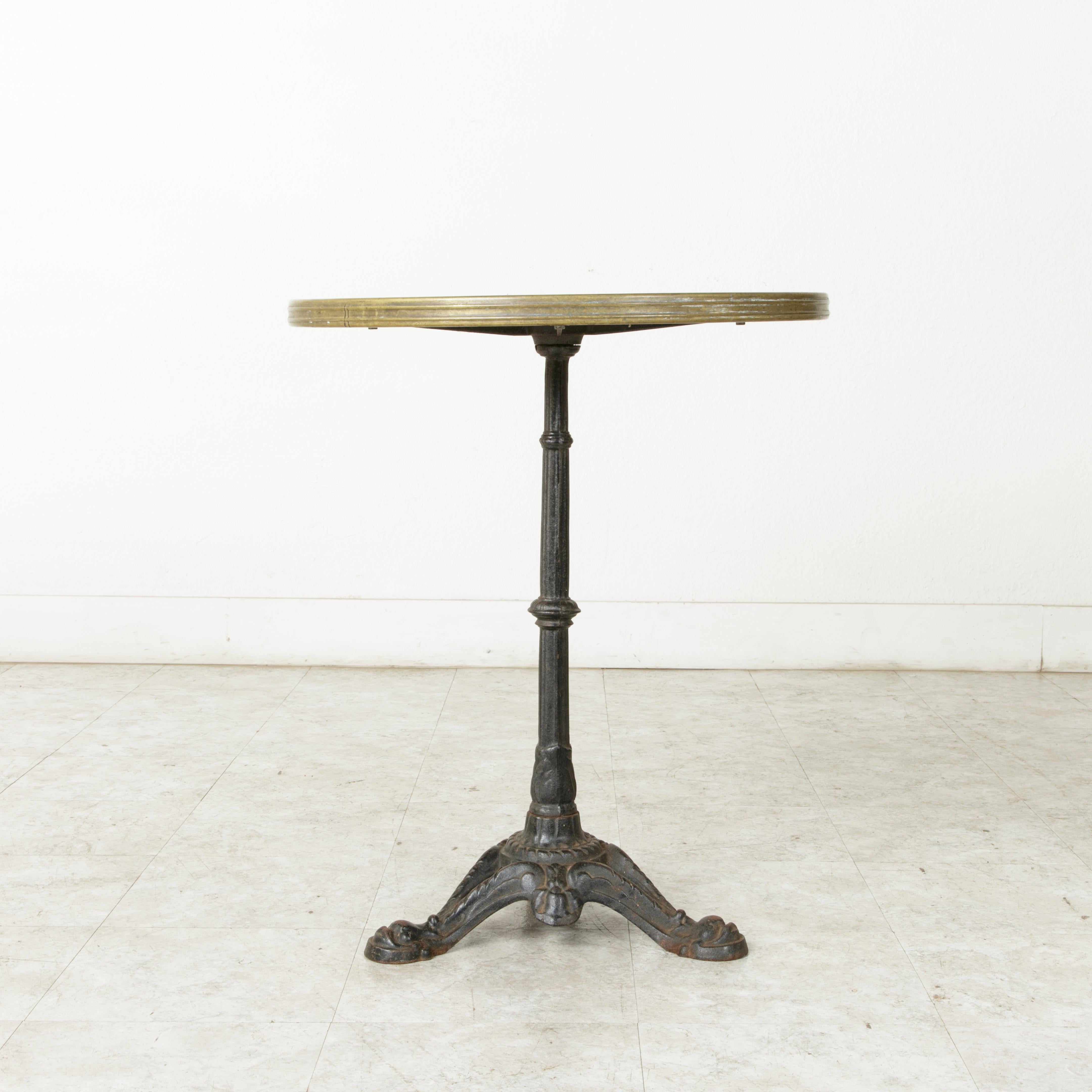 This midcentury French bistro table features a cast iron base detailed with fluting and stylized dolphin heads. Its generous 23.75 inch diameter Formica top is larger than its earlier counterparts and is trimmed with brass banding. Reminiscent of