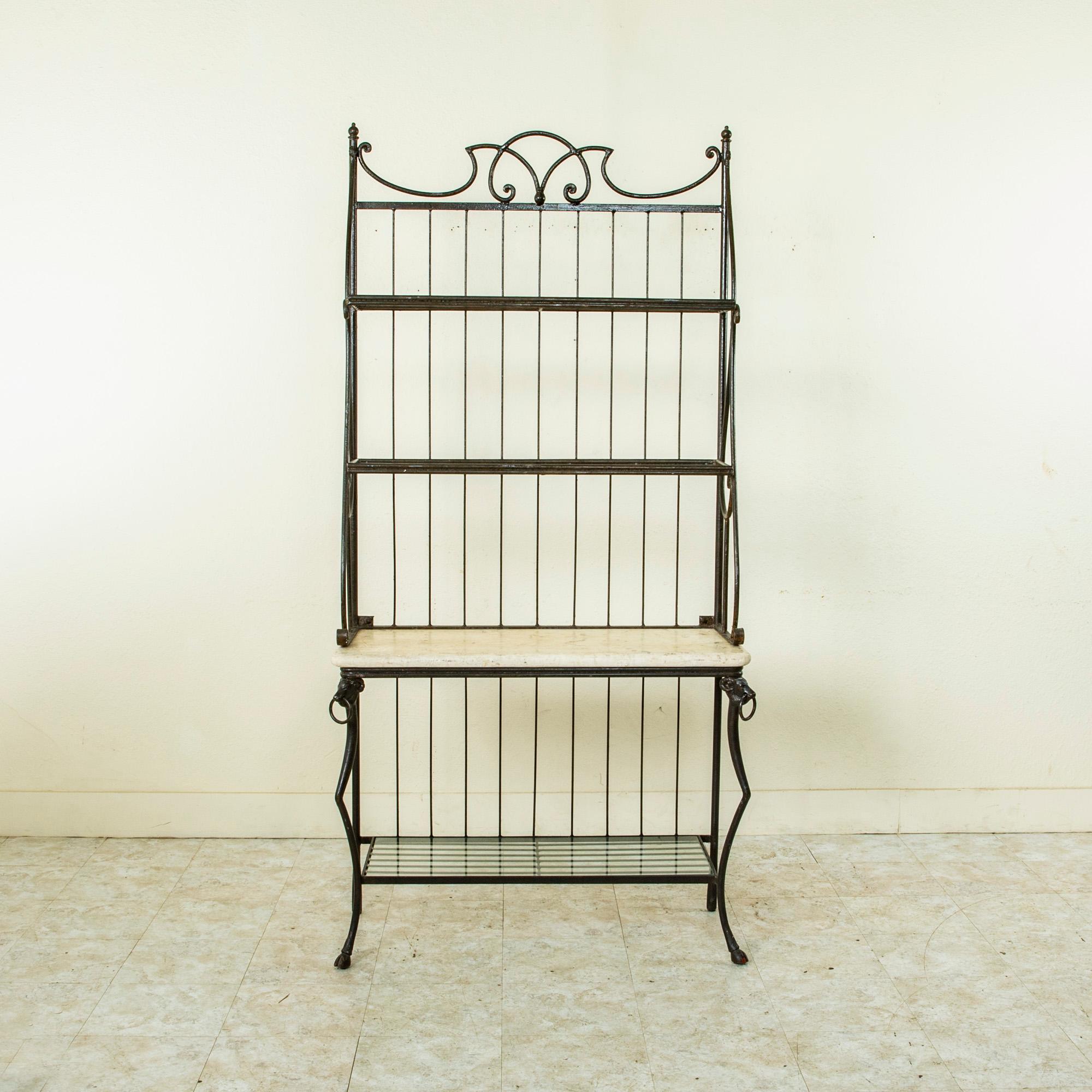 Originally used in a French butcher shop, this iron butchers rack features ram's heads and cloven feet on the base. The base is fitted with a stone top and a lower glass shelf, while the upper section is fitted with two more glass shelves. The piece