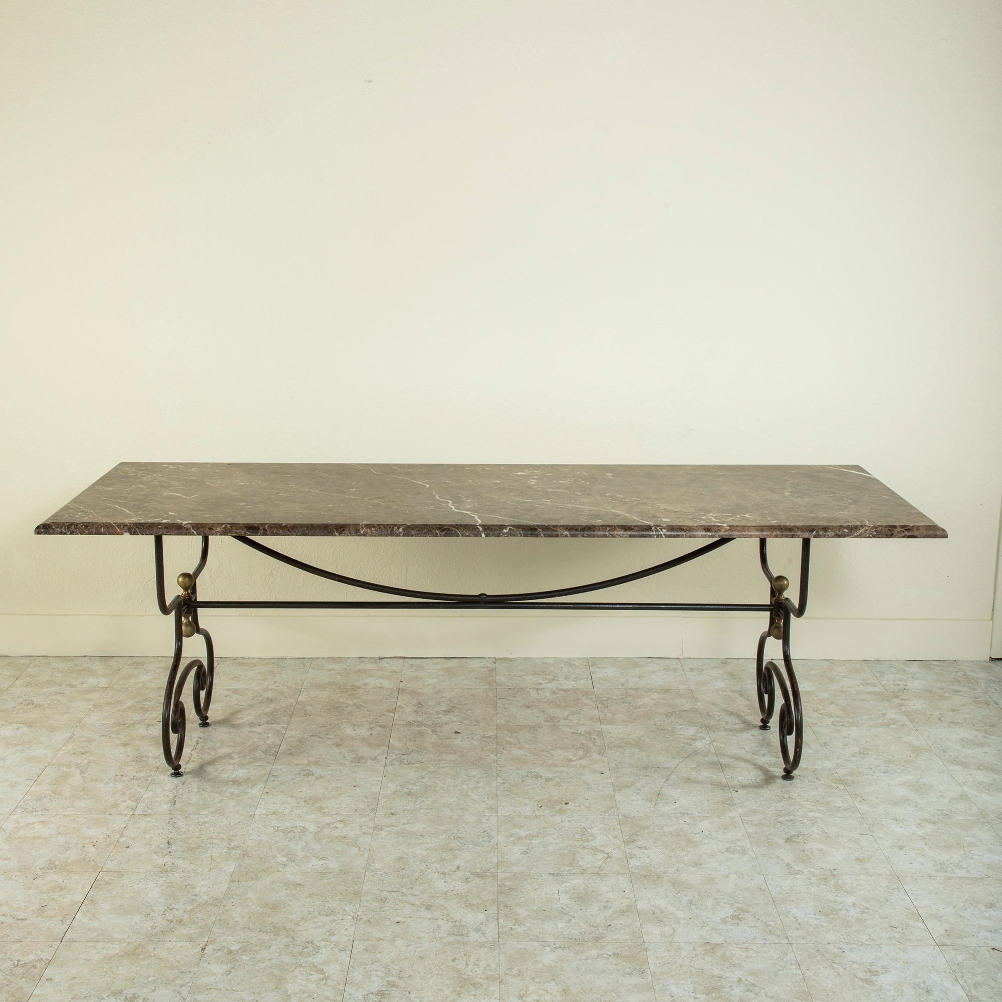 This mid-twentieth century French iron dining table features an 86 inch long beveled marble top. The marble top rests on a scrolled iron base detailed with bronze finials. An iron stretcher joins the legs and provides additional stability. An ideal