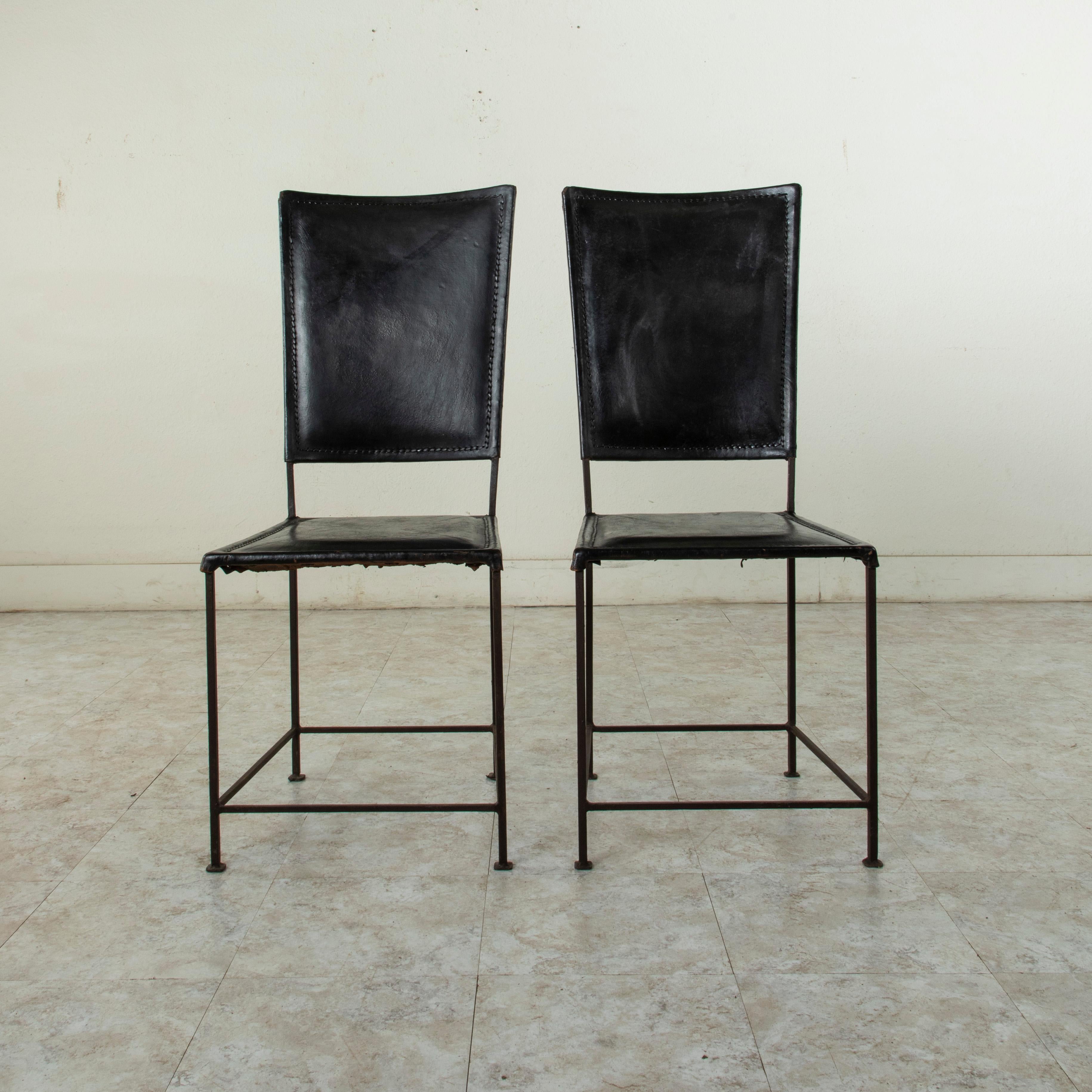 This handsome pair of French iron chairs from the mid-twentieth century features black leather seats and backs. The tall tapered seat backs have a gentle incline. Iron supports on all four sides join the legs. Simple in form, this pair would blend