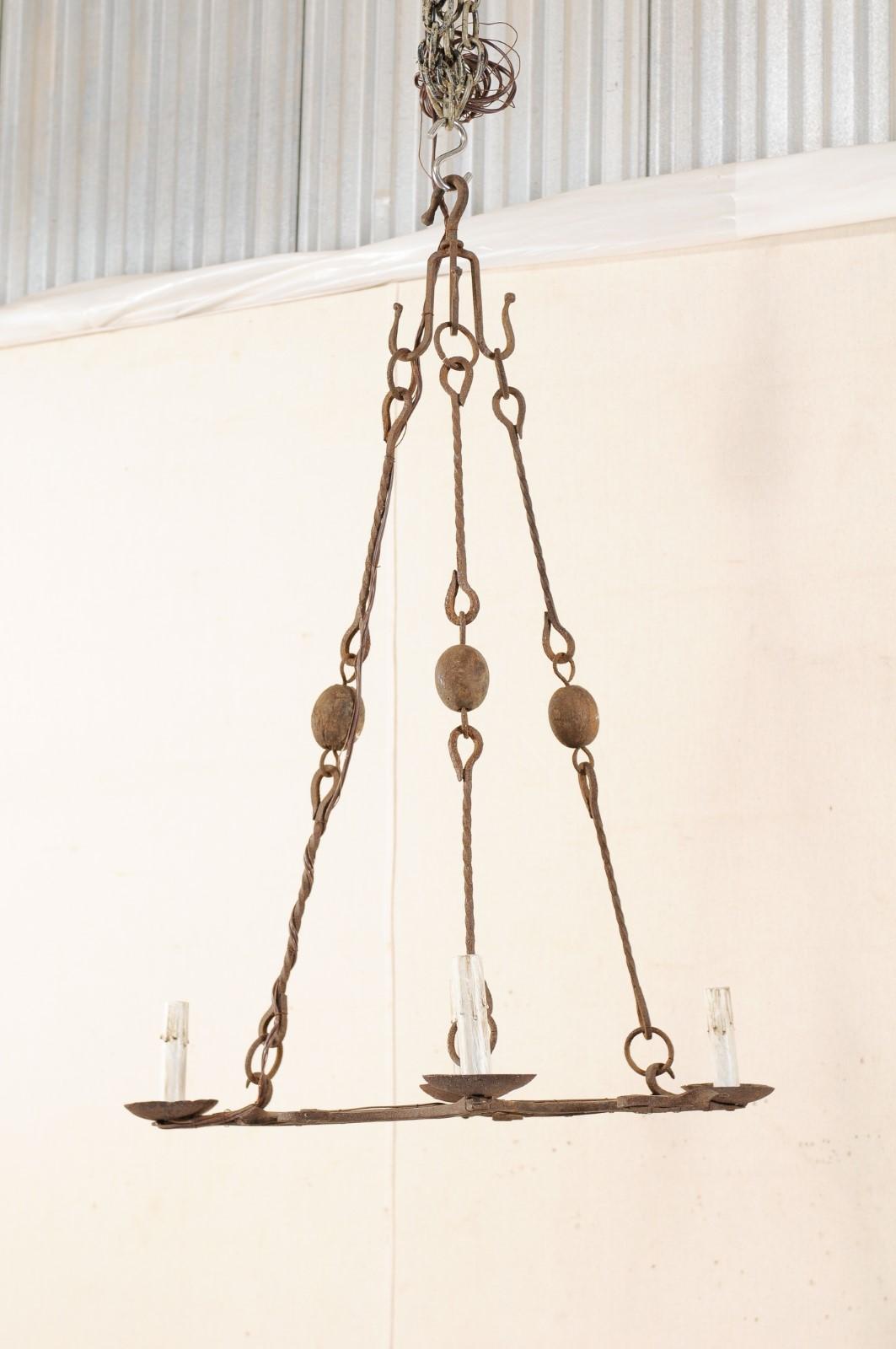 A French four-light iron chandelier from the mid-20th century. This vintage hanging light-fixture from France has an overall rectangular-shaped center (when viewed from beneath), each side adorn with a pair of iron bars that project outward, joining