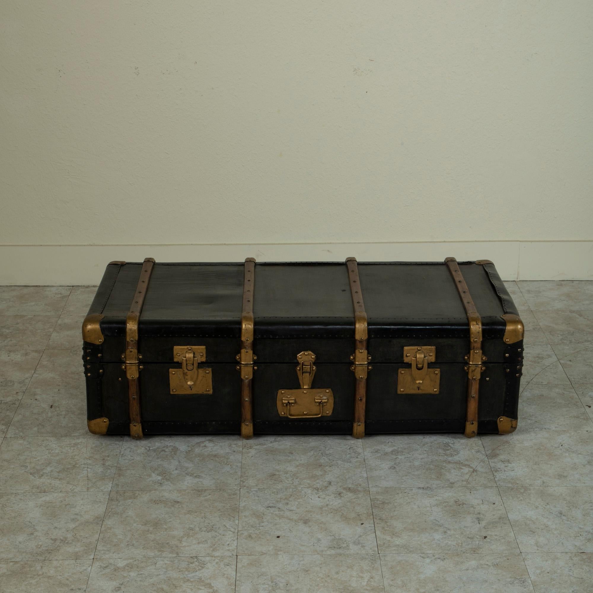This French steam trunk from the mid-twentieth century is covered in black leather and moleskin and features wooden runners and metal corners painted gold. On one side is a brass plate where a card with one's name and address can be inserted, as