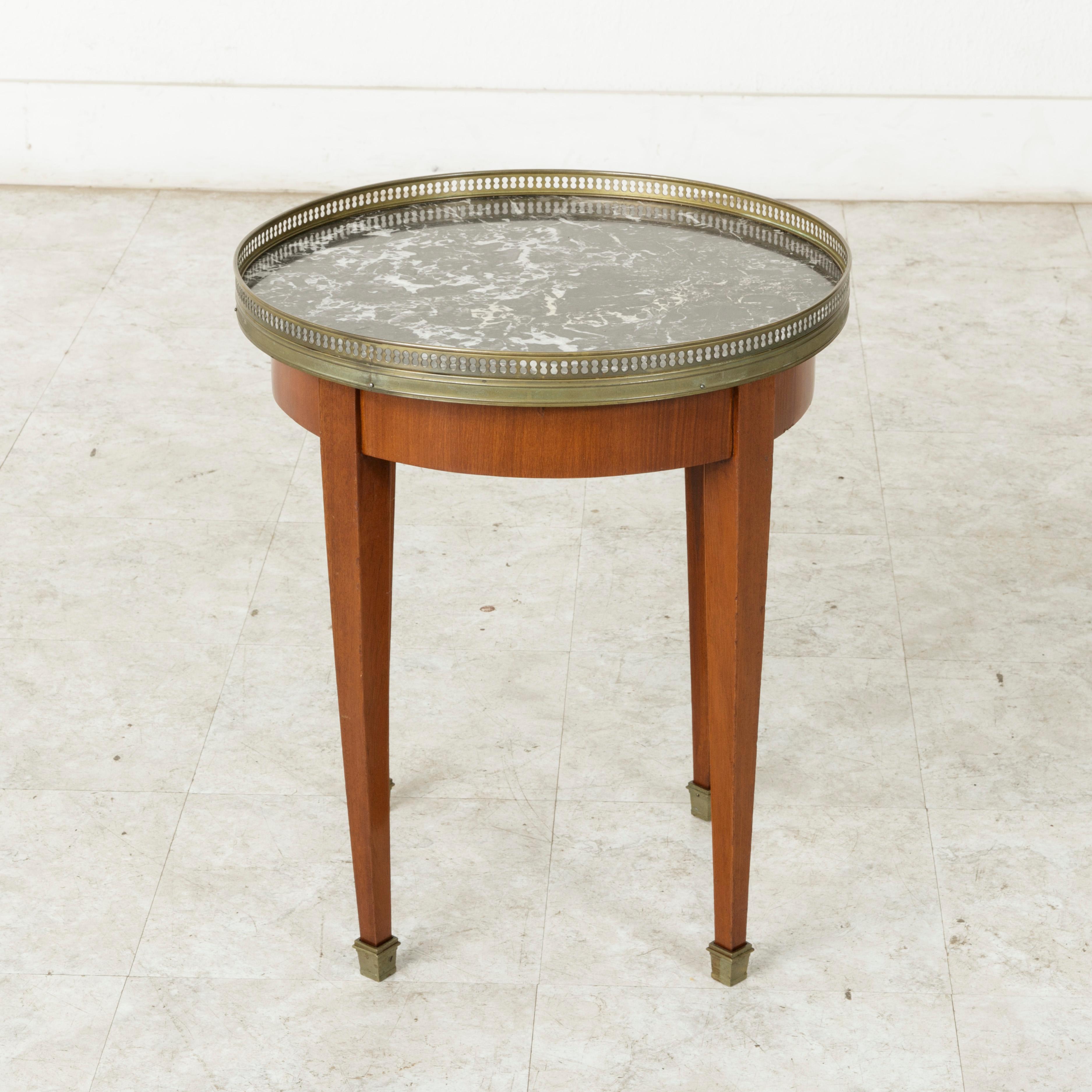 This mid-20th century French Louis XVI style cherrywood side table features a Saint Anne marble top surrounded by a pierced brass gallery. The tabletop rests on four tapered square legs finished with brass sabots. An ideal table beside a chair,