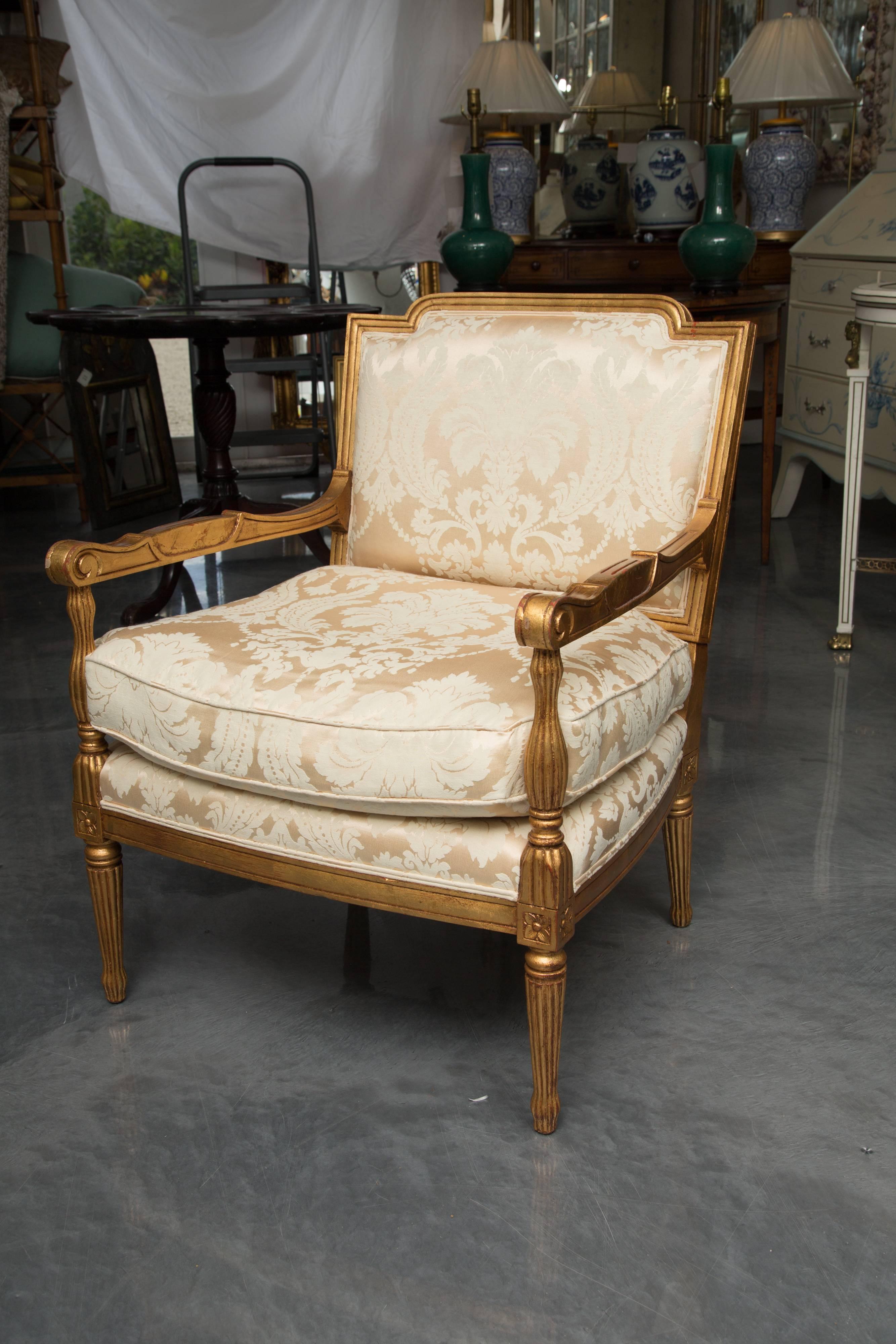 This is an interesting pair of stylized giltwood French Louis XVI stylized armchairs. The dog-eared top rail is over a fully upholstered back and an upholstered loose cushion seat flanked by out-scrolled arms. The chairs are supported by round