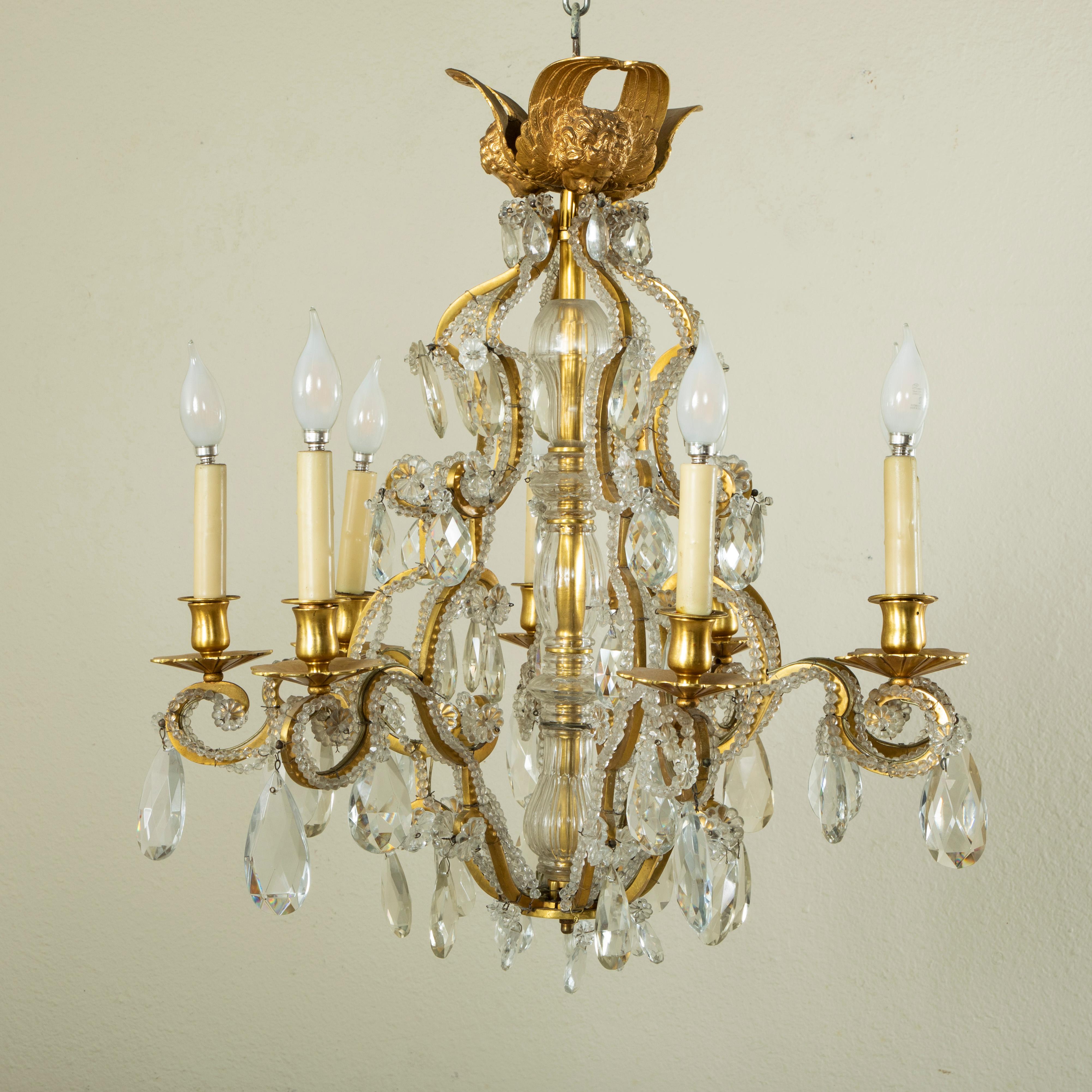 From the mid-twentieth century, this beautiful gilt bronze chandelier features eight elegantly curved arms lined with beaded crystals, which extend from a tall central glass column. The chandelier is appointed with crystal faceted pear drops,