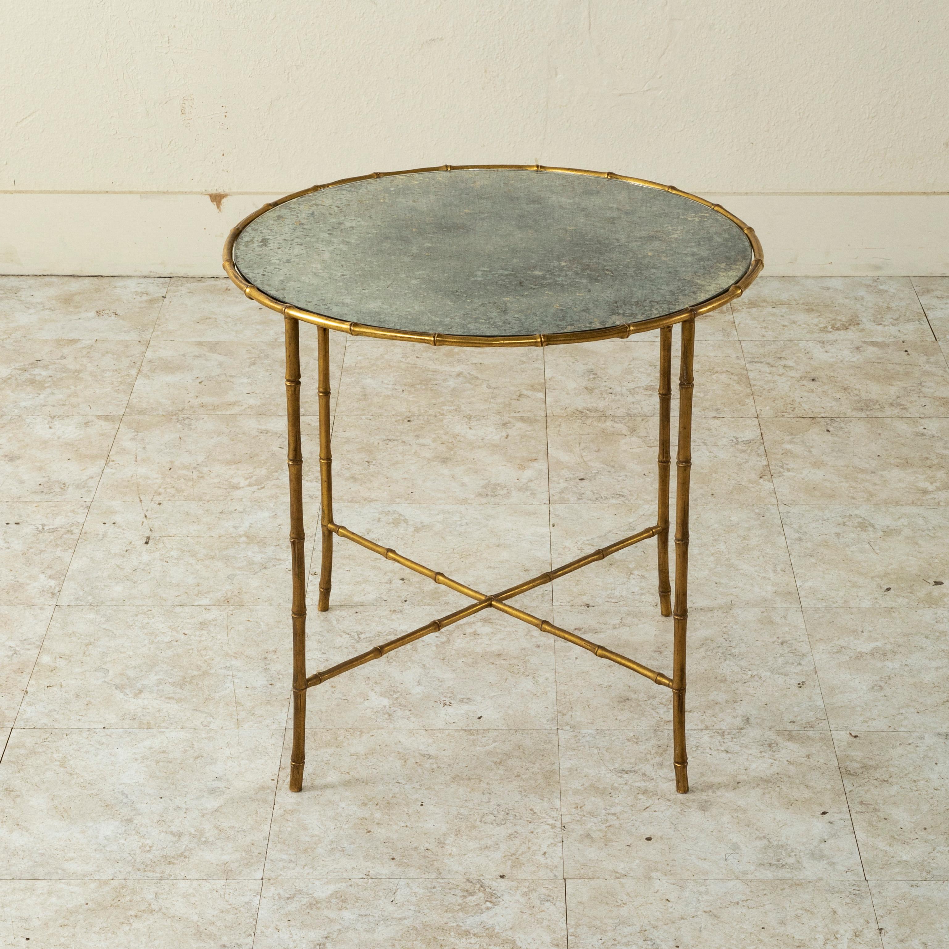 This mid-century French Maison Bagues round side table or coffee table features a faux bamboo bronze frame. The table is fitted with its original mirrored glass top. A small scale cocktail table to mix with contemporary interiors. c. 1960.