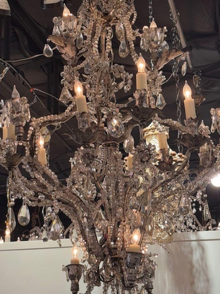 Crafted with the elegance of yesteryear, this Mid 20th Century French Maison chandelier is a stunning example of classic design meeting timeless allure. The piece features a sophisticated palette of gilt silver tole, complemented by the chandelier's