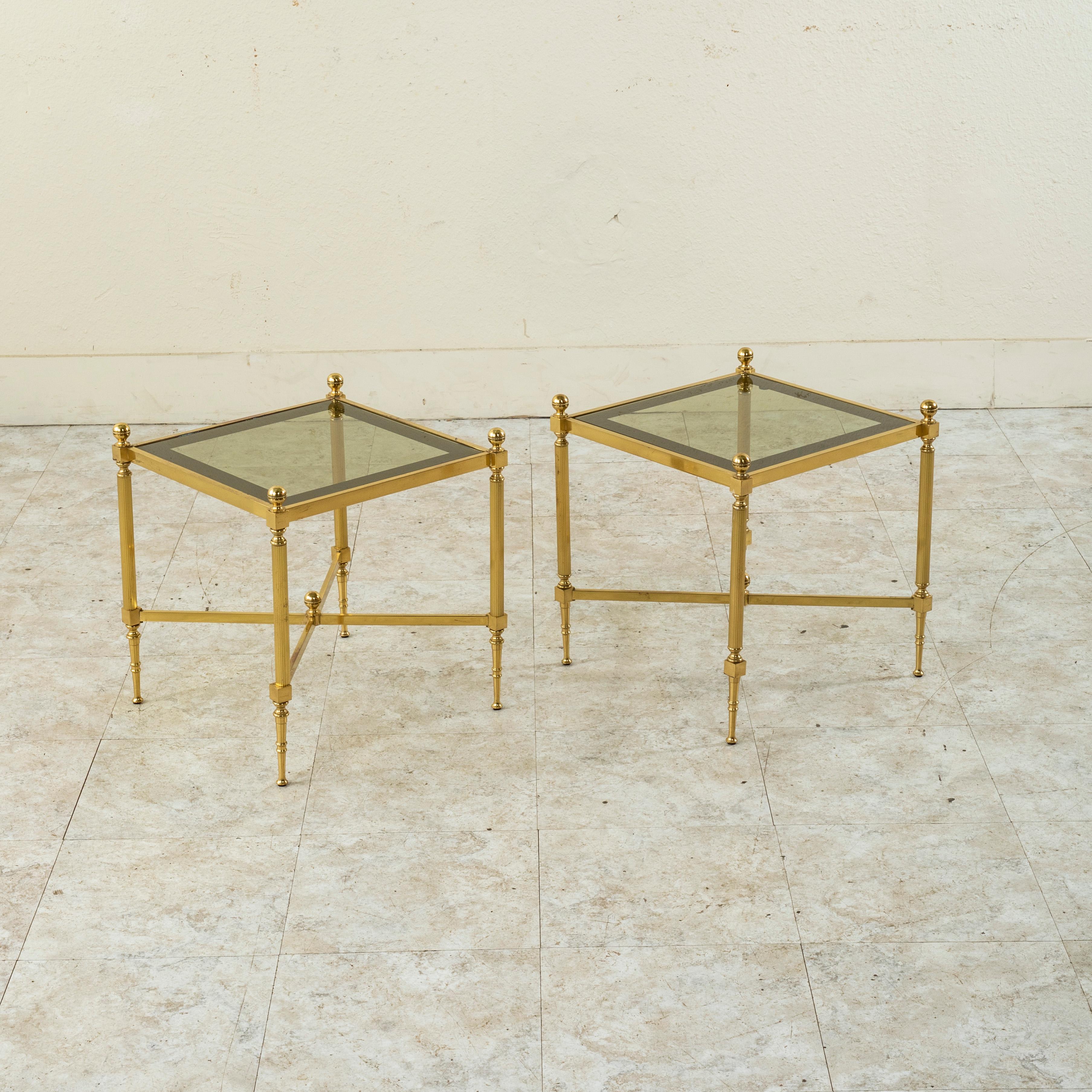 This pair of mid-century Maison Jansen brass side tables features glass tops with tinted edges. The tables are detailed with fluted legs, finials, and a lower X stretcher with a central finial. c. 1960.