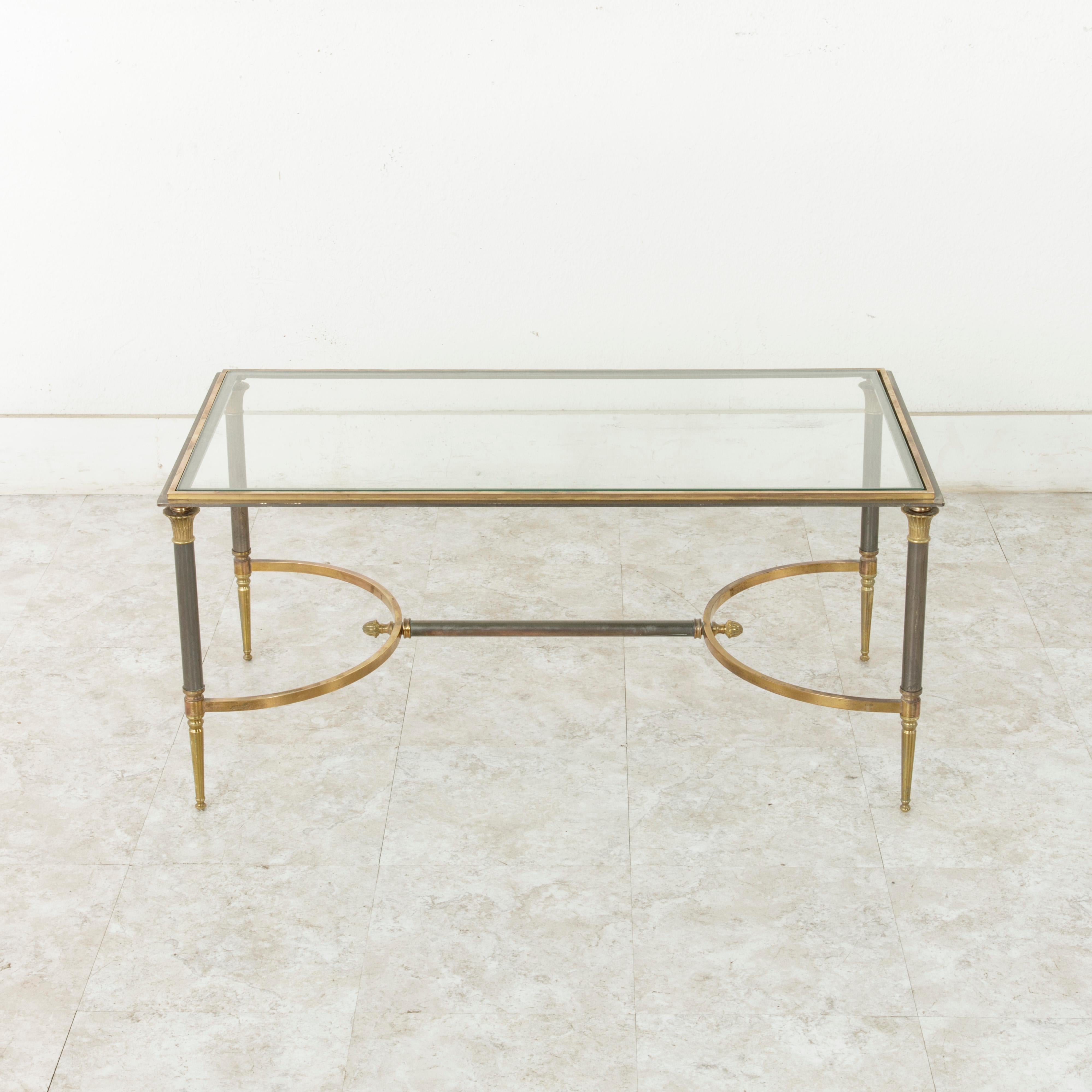 This midcentury French brass and iron coffee table or cocktail table by Maison Jansen is inspired by the Directoire style with its Egyptian style capitals at the top of each leg. The base is joined by an H stretcher with half circles on each side