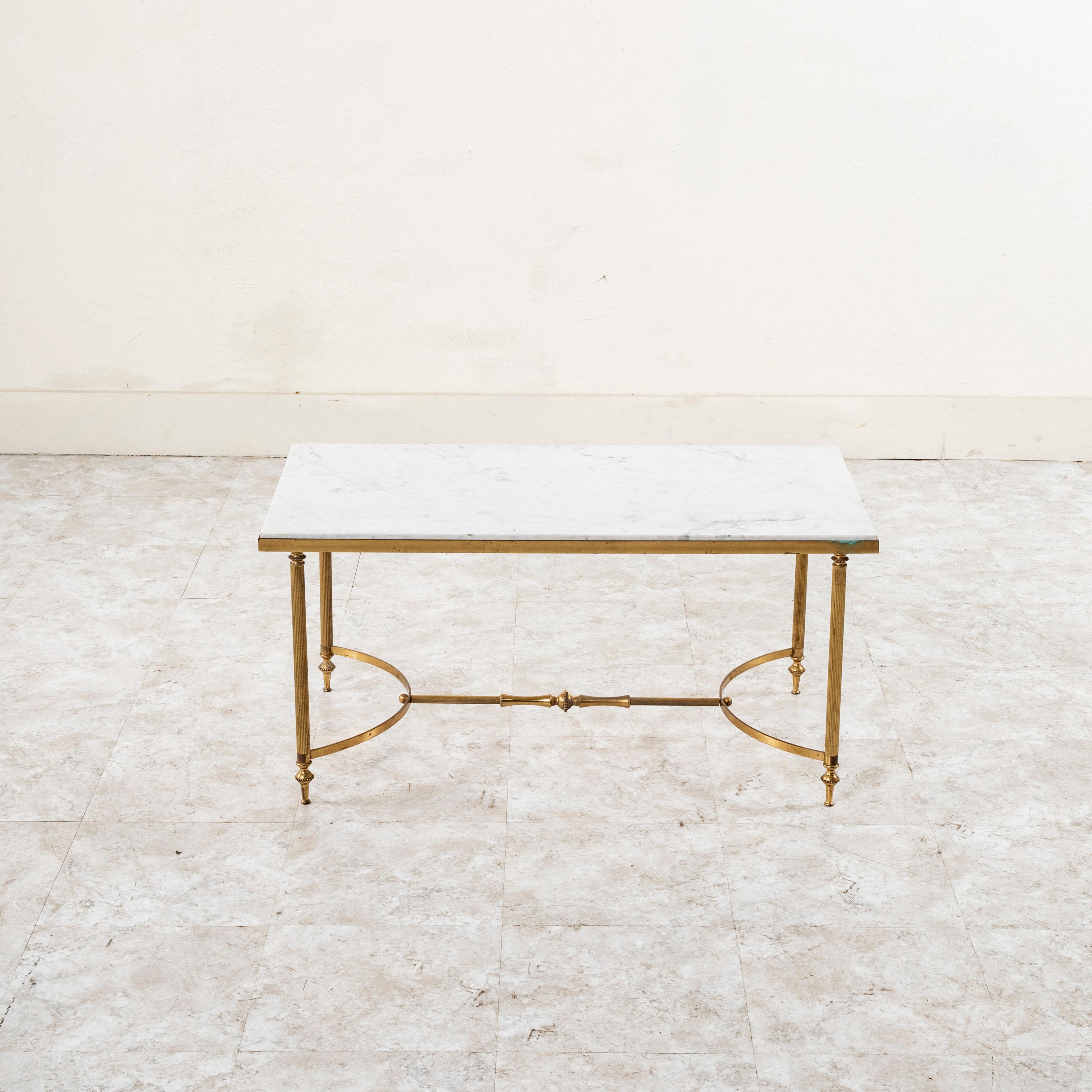 This midcentury French brass coffee table or cocktail table features a solid white marble top. The base is joined by an H stretcher with half circles on each side held firmly in place by a central rod finished with a finial at each end. Its four