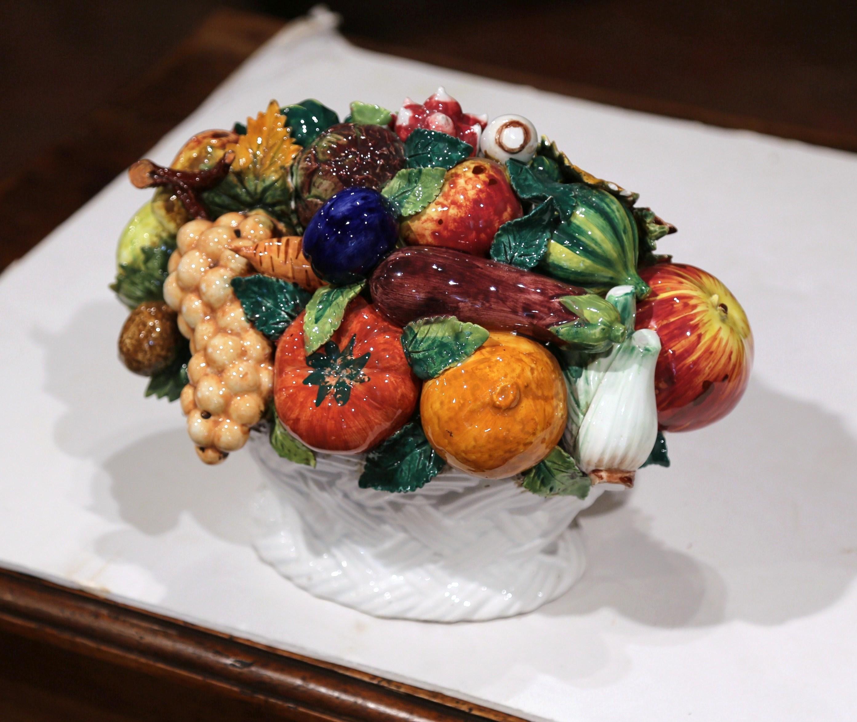 Dekorieren Sie einen Tisch mit dieser farbenfrohen Korbkomposition aus Majolika. Der um 1950 in Frankreich gefertigte Tafelaufsatz zeigt eine realistische Auswahl an Früchten und Gemüsen im Hochrelief in einem weißen Korb in Flechtform. Das