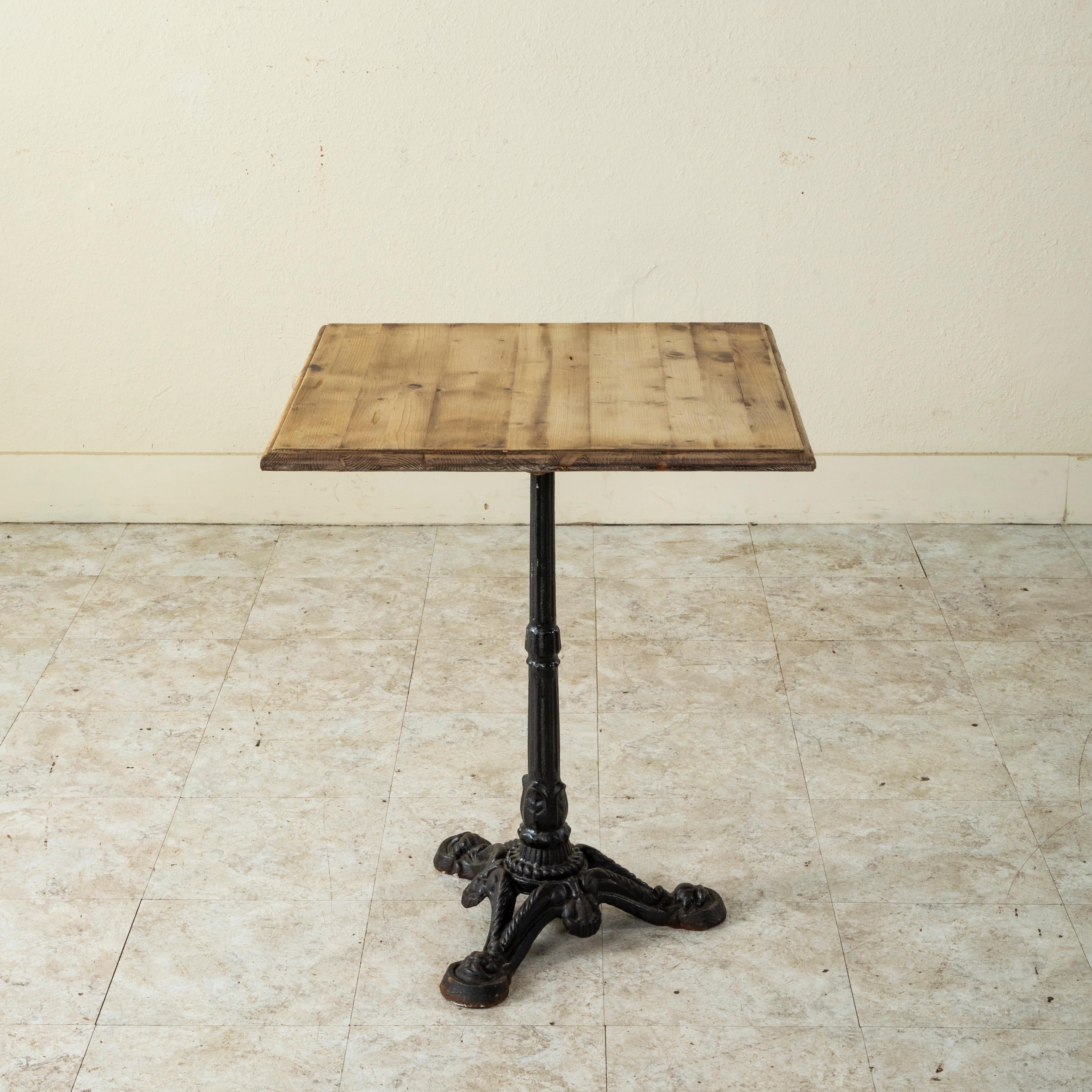 Originally used in a French brasserie from the mid-twentieth century, this cast iron bistro table or cafe table features features a cast iron pedestal base and a 24-inch square bleached pine top. The fluted pedestal rests on three feet detailed with