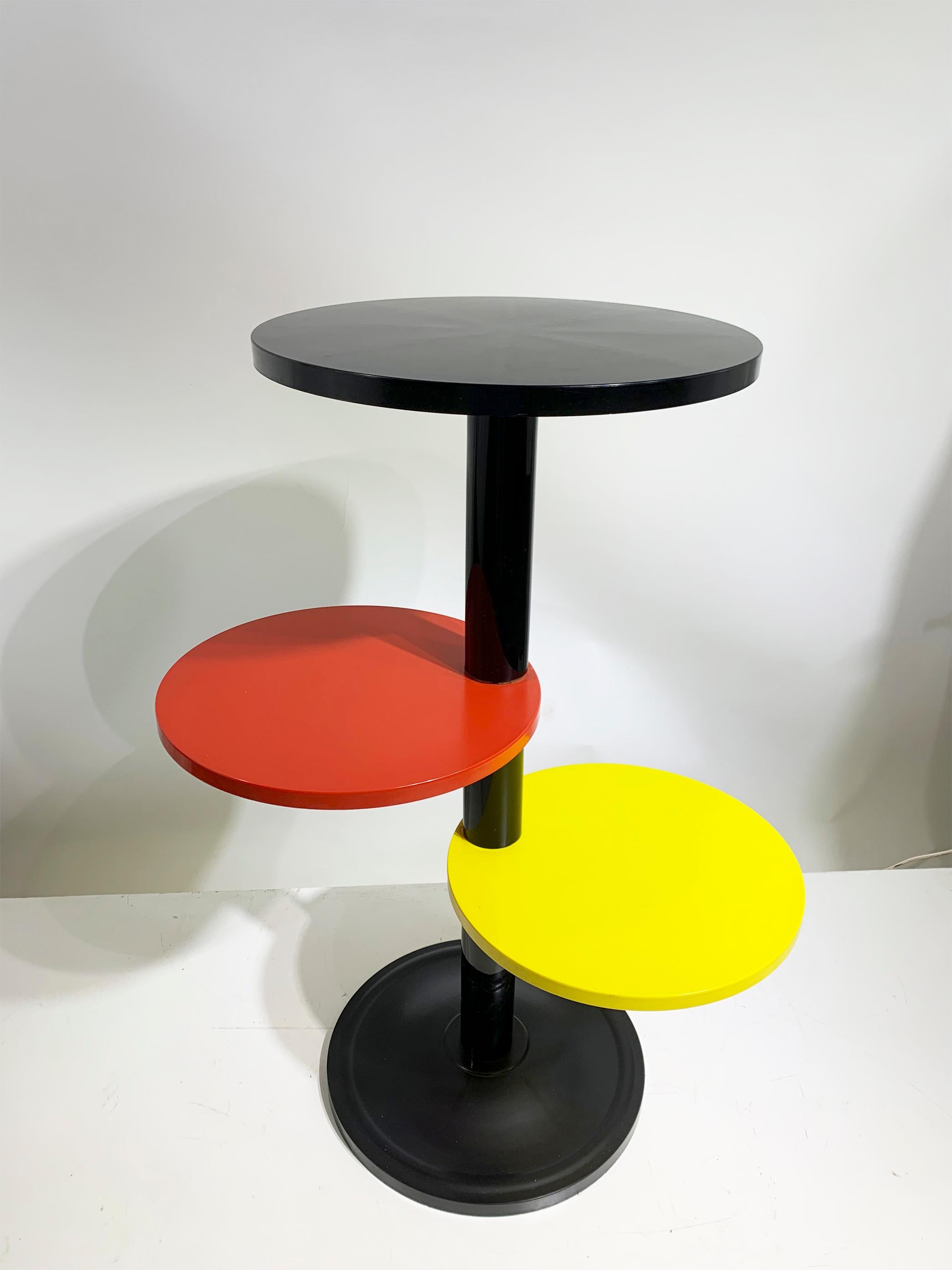 This delightful French plastic table/plant stand, originating from the 1960s, exudes retro charm with its clever design. Featuring circular shelves in striking black, red, and yellow hues, each one playfully offset from the central column, this